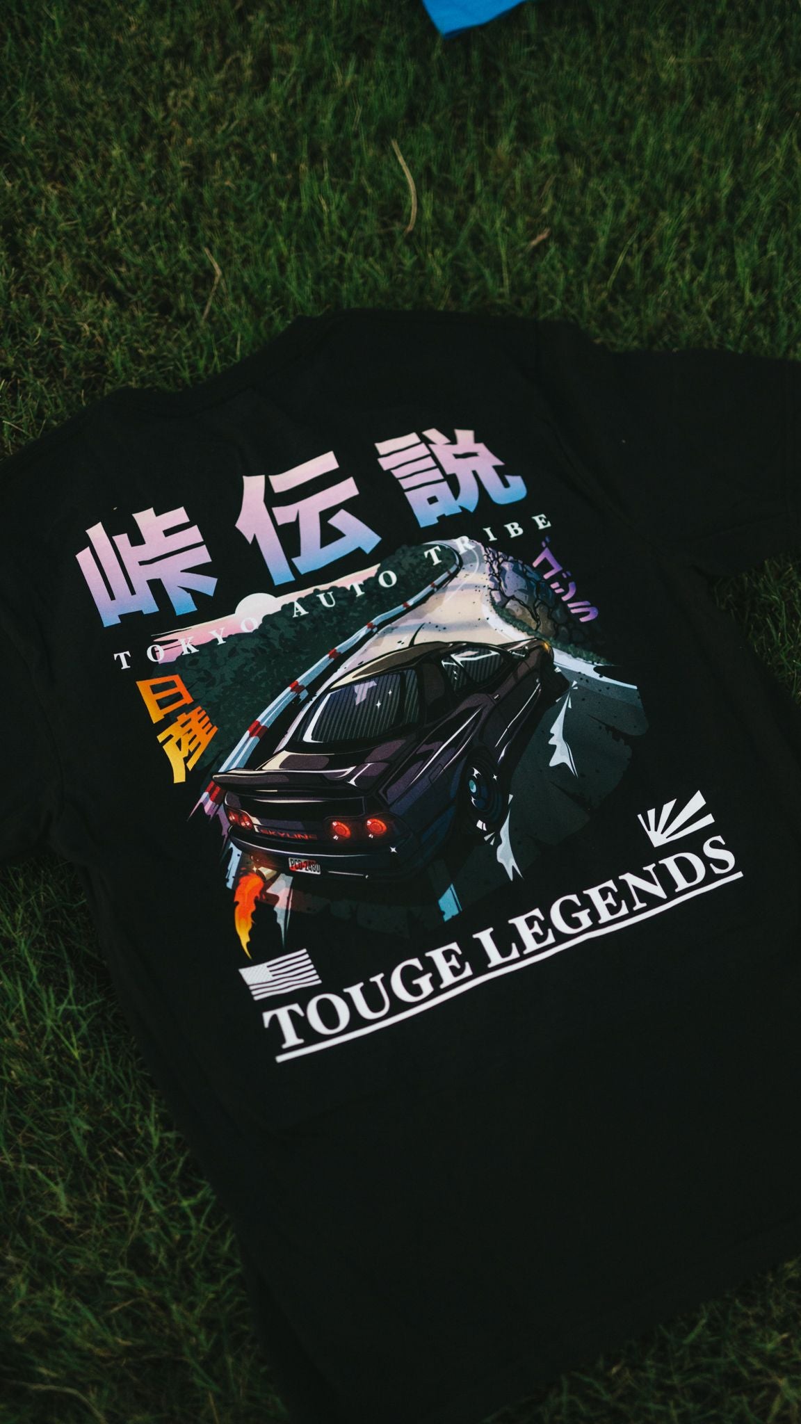 Black graphic tee featuring a detailed illustration of a drifting Nissan on a mountain touge road with Japanese text and "Touge Legends (more colors)" branding, capturing the spirit of late-night JDM streetwear culture.