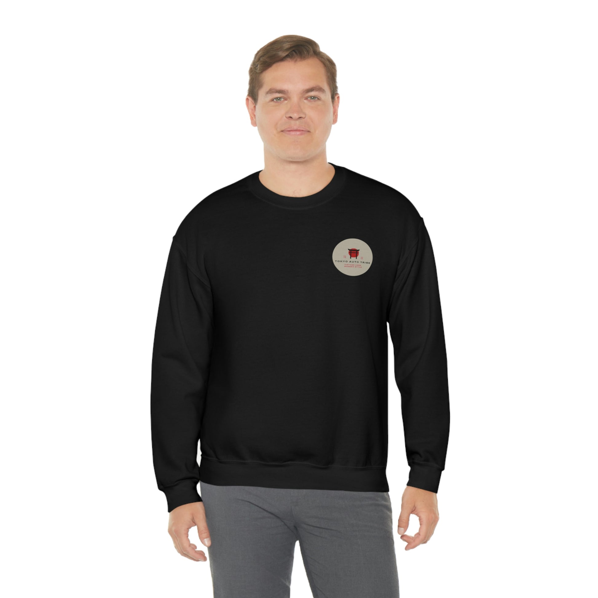 A man wearing The Family Wagon Sweater in black featuring a small circular vintage car culture graphic on the chest, blending JDM streetwear with automotive nostalgia.