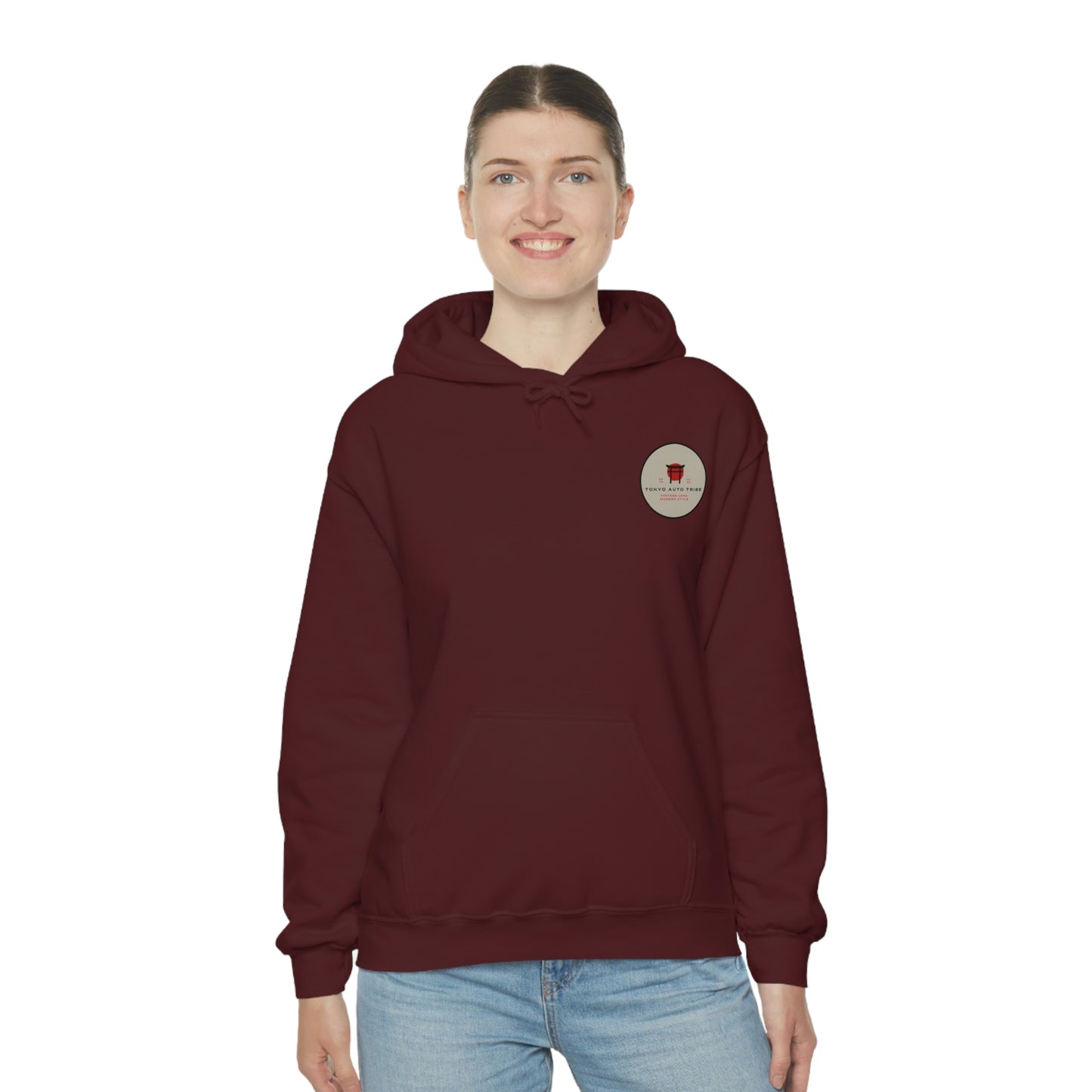 A woman wearing a maroon Groovy Grocery Runner Hoodie featuring a small circular graphic on the chest, styled with casual blue jeans, embodying Japanese car culture and late-night drives.