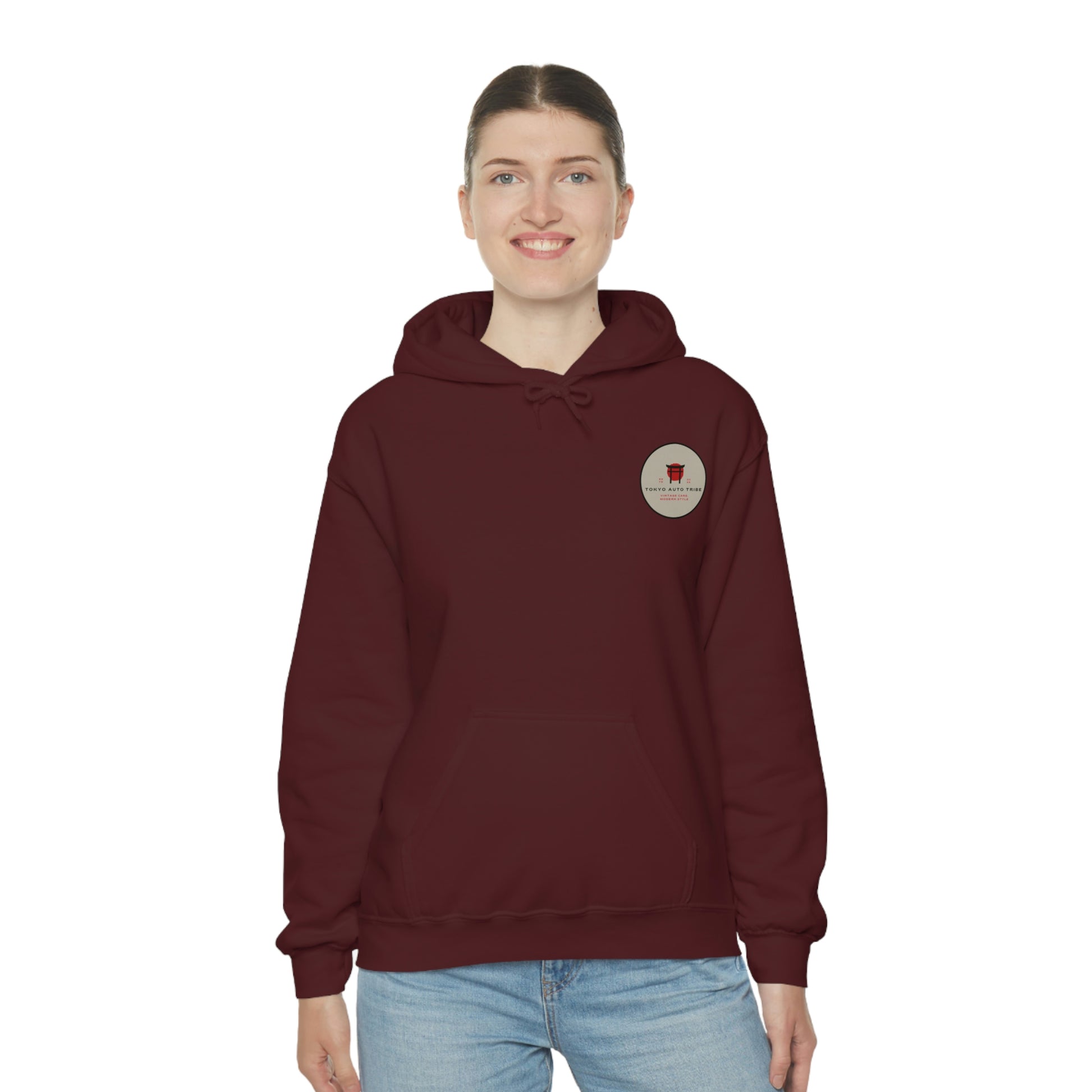 A woman wearing a maroon Groovy Grocery Runner Hoodie featuring a small circular graphic on the chest, styled with casual blue jeans, embodying Japanese car culture and late-night drives.