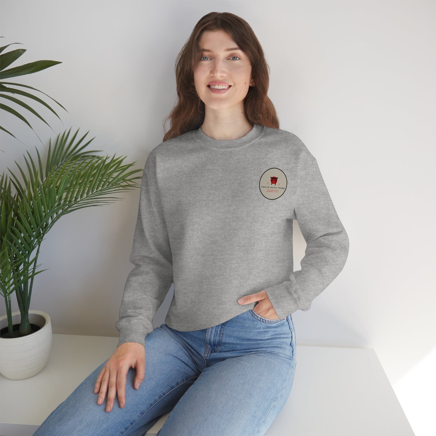Smiling woman wearing a grey Wagon Chibi Sweater sitting indoors next to a potted plant, embodying the casual comfort and Japanese car culture vibe inspired by Tokyo Auto Tribe.
