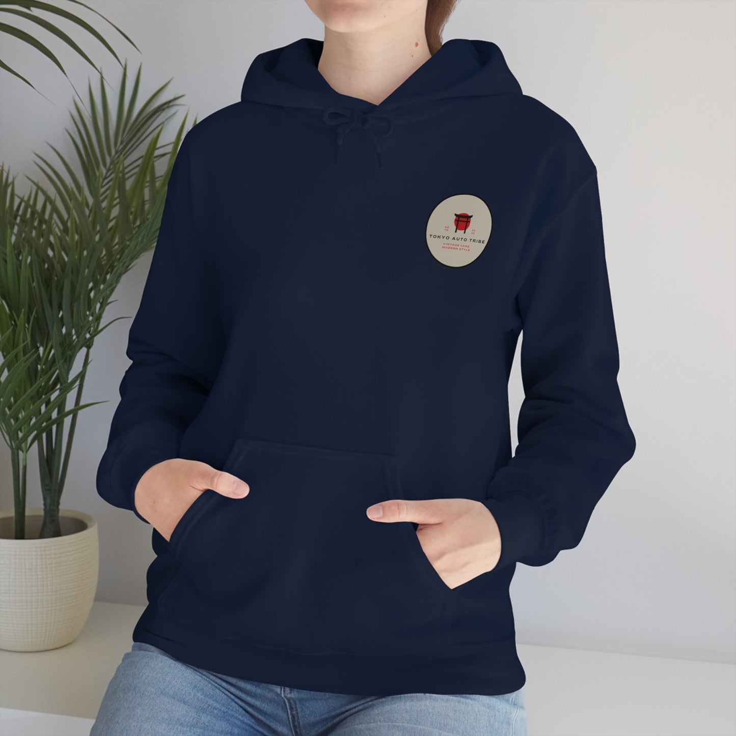 A person wearing a navy blue Wagon Chibi Hoodie with a small circular graphic logo on the left chest, styled casually with hands in the front pocket, set against a minimal indoor background.