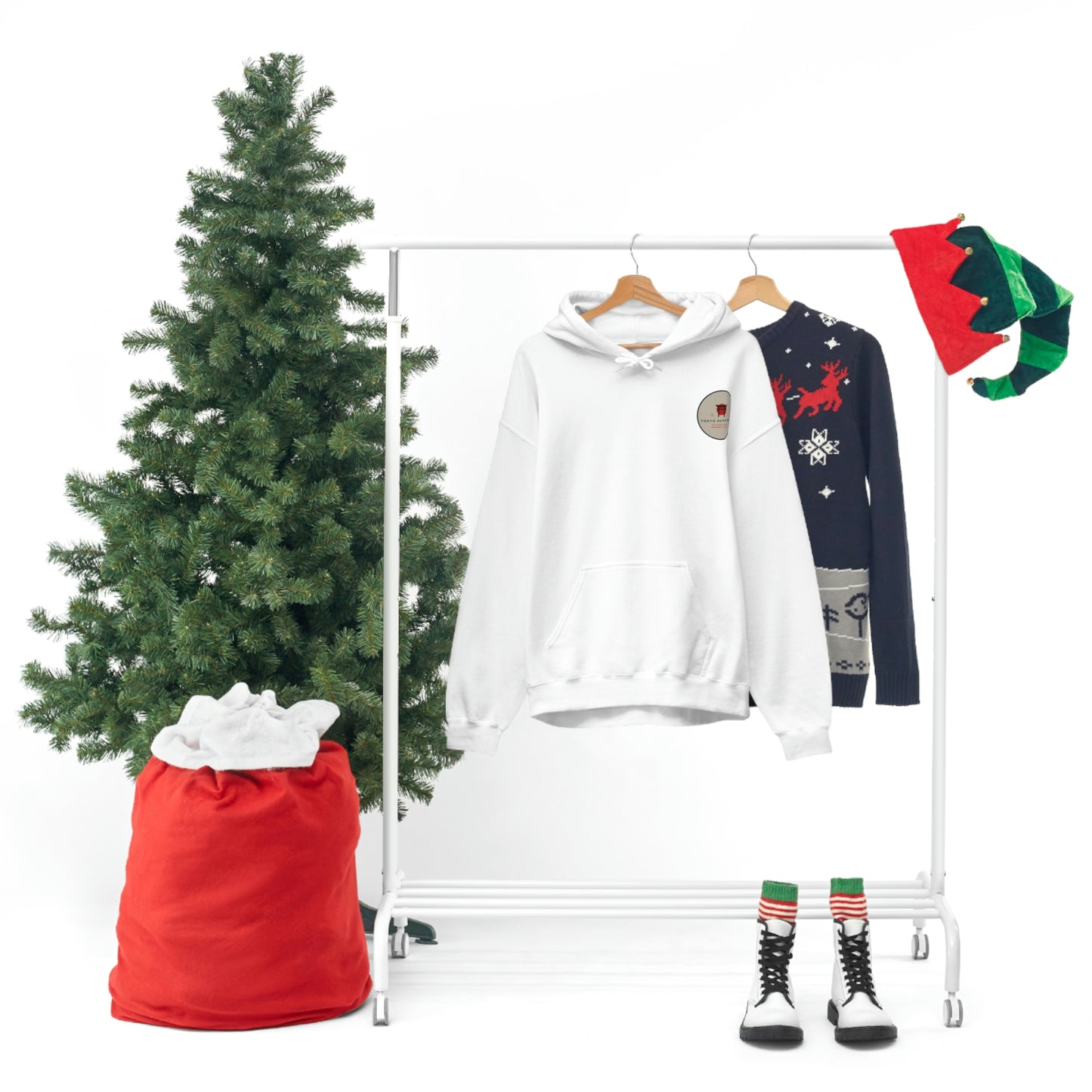 White Groovy Grocery Runner Hoodie hanging next to a holiday-themed sweater on a rack, accompanied by festive Christmas decorations including an evergreen tree and red sack.