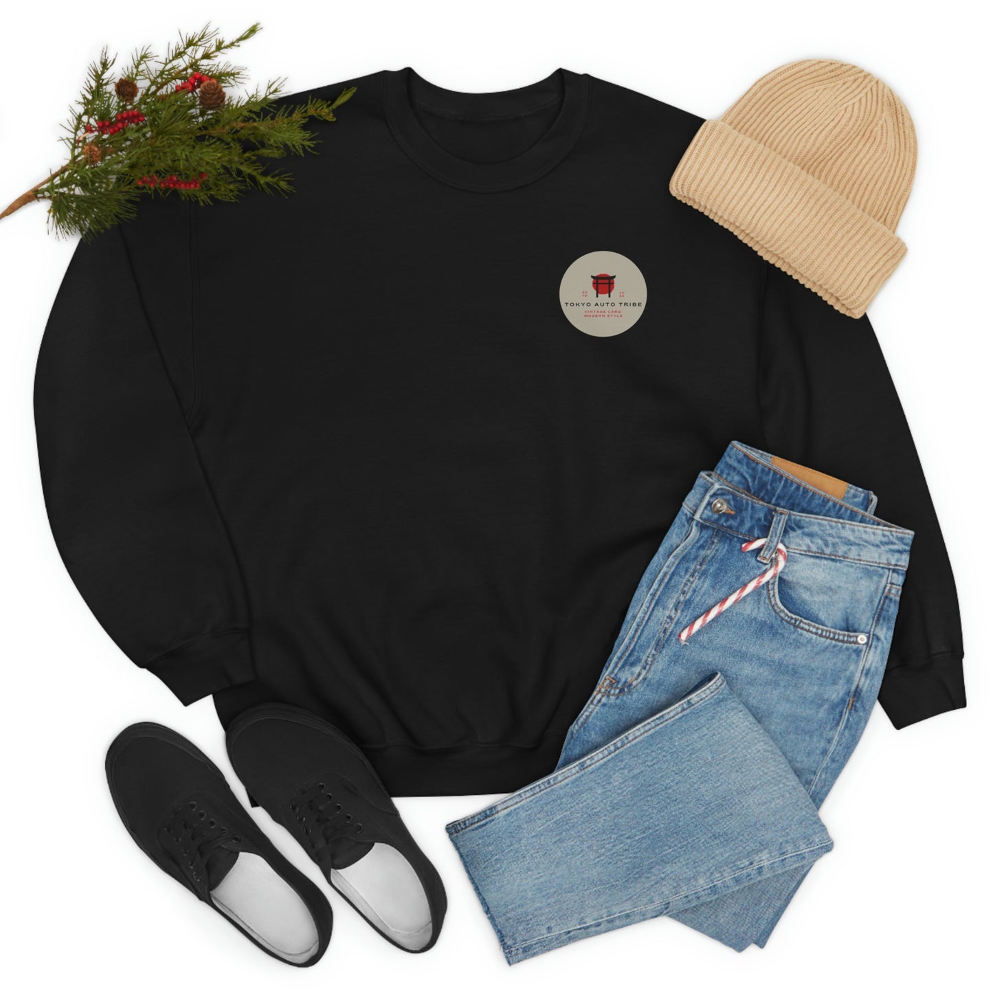 The Family Wagon Sweater in black with a small round Tokyo Auto Tribe emblem, styled with light blue jeans, black sneakers, a beige knit beanie, and festive greenery for a casual Japanese car culture-inspired look.