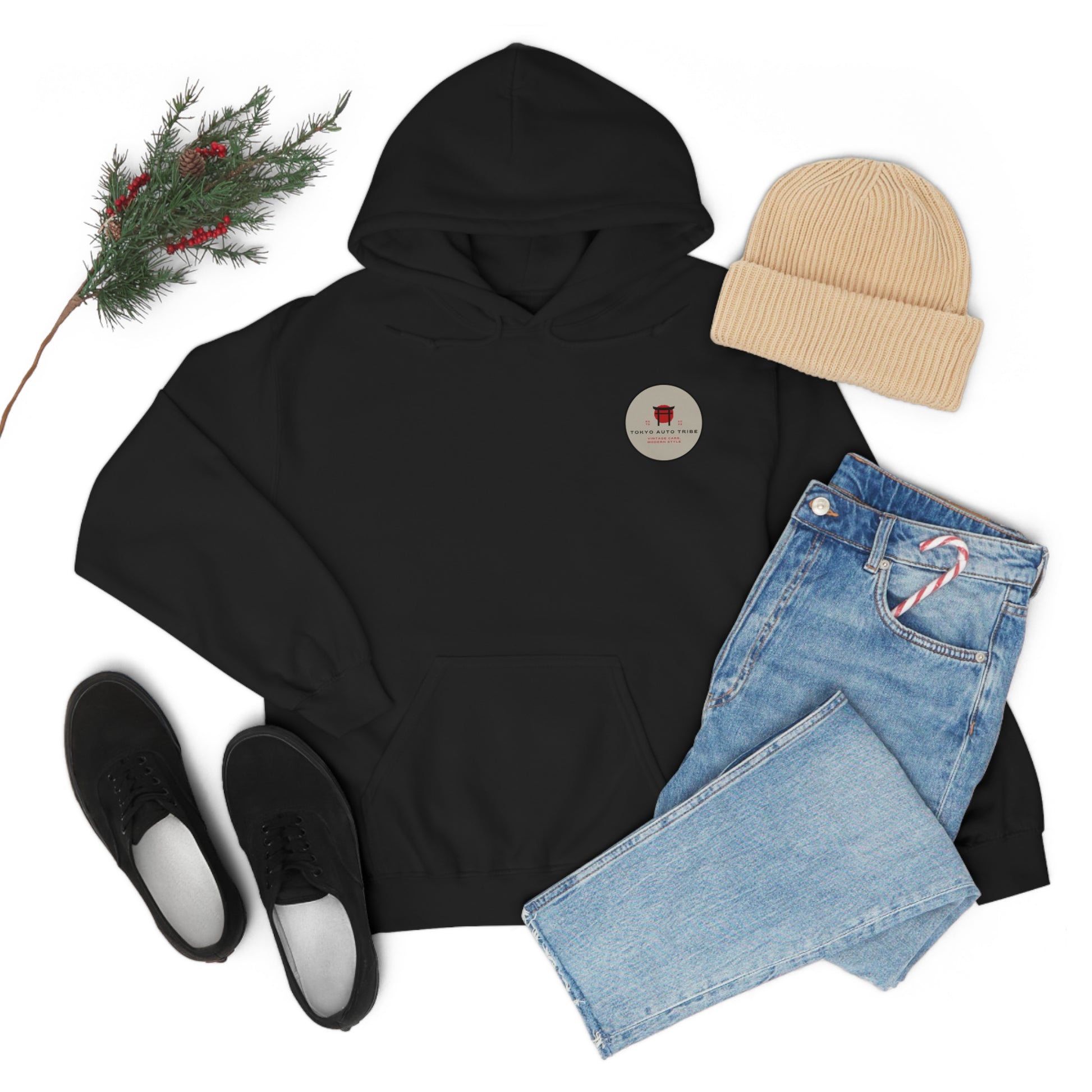 Black Wagon Chibi Hoodie laid flat with light wash jeans holding a candy cane, beige knit beanie, black sneakers, and a sprig of pine with red berries, evoking cozy JDM streetwear style.
