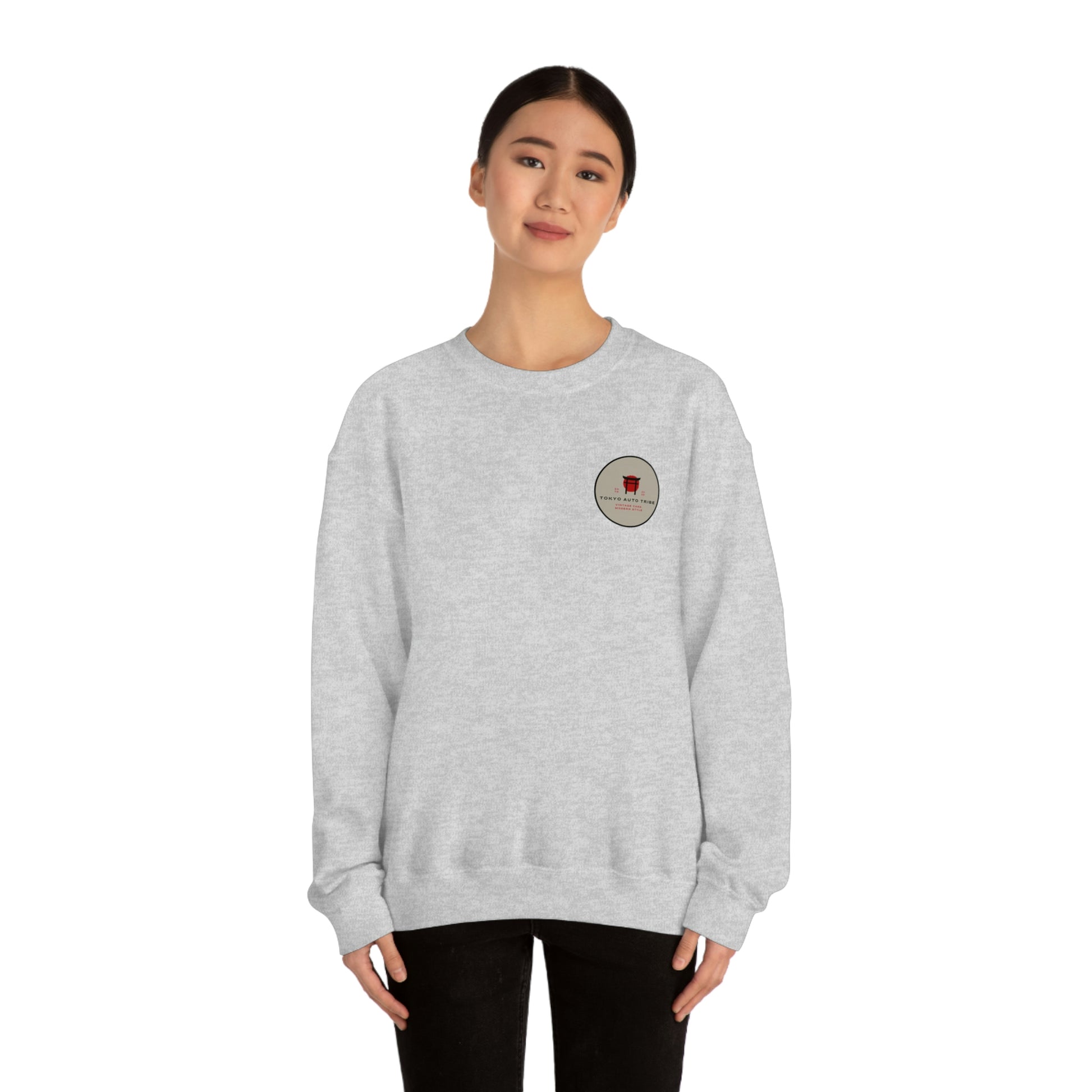 Woman wearing a light gray sweatshirt featuring a small round graphic on the chest that reads Tokyo Auto Tribe, styled as The Family Wagon Sweater, blending JDM streetwear with Japanese car culture.