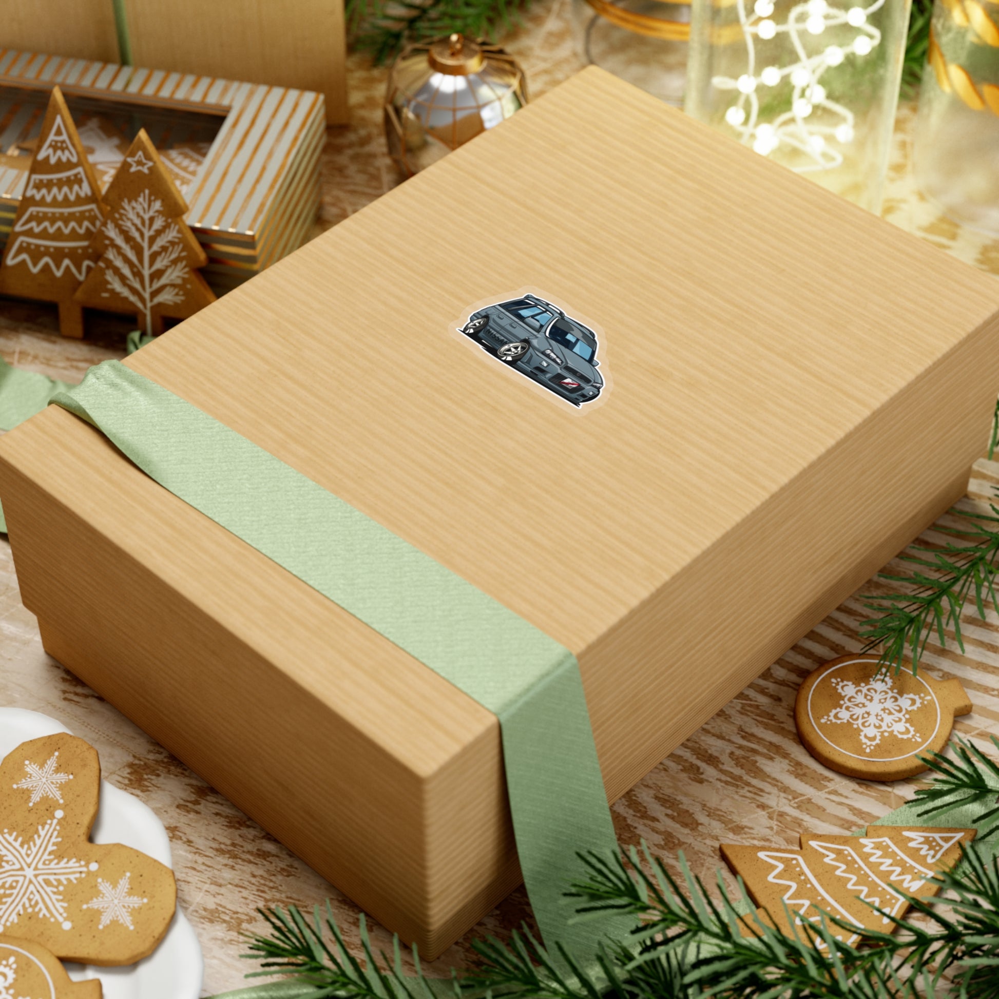 A kraft gift box wrapped with a green ribbon featuring a small Wagon Wonder Sticker of a detailed blue vintage car, surrounded by holiday-themed gingerbread cookies and festive decor.