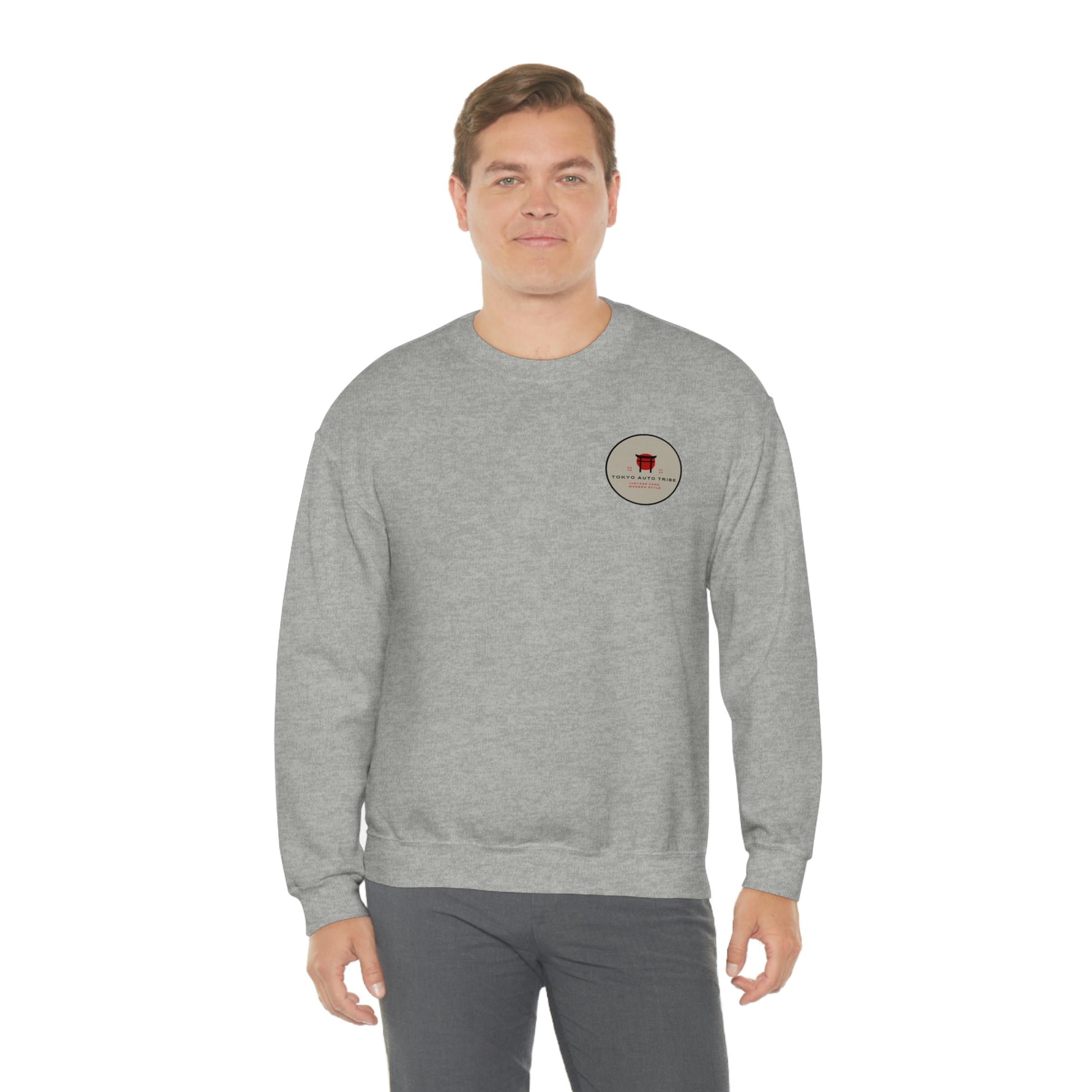 A man wearing a light gray crewneck sweatshirt featuring a small Tokyo Auto Tribe graphic on the chest, representing The Family Wagon Sweater, built for fans of Japanese car culture and late-night drives.