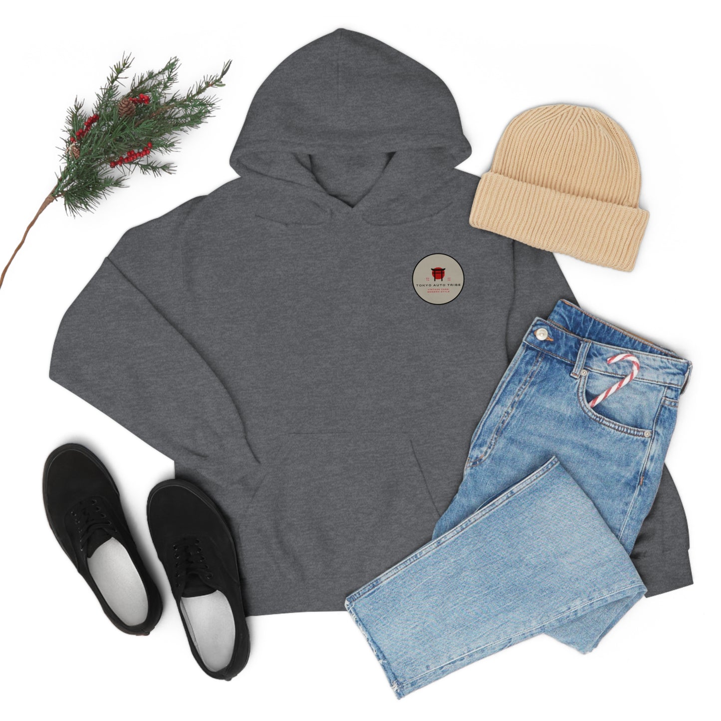 Flat lay of a dark gray Wagon Chibi Hoodie paired with light blue jeans, black sneakers, a beige knit beanie, and a sprig of pine with red berries, evoking cozy winter streetwear.