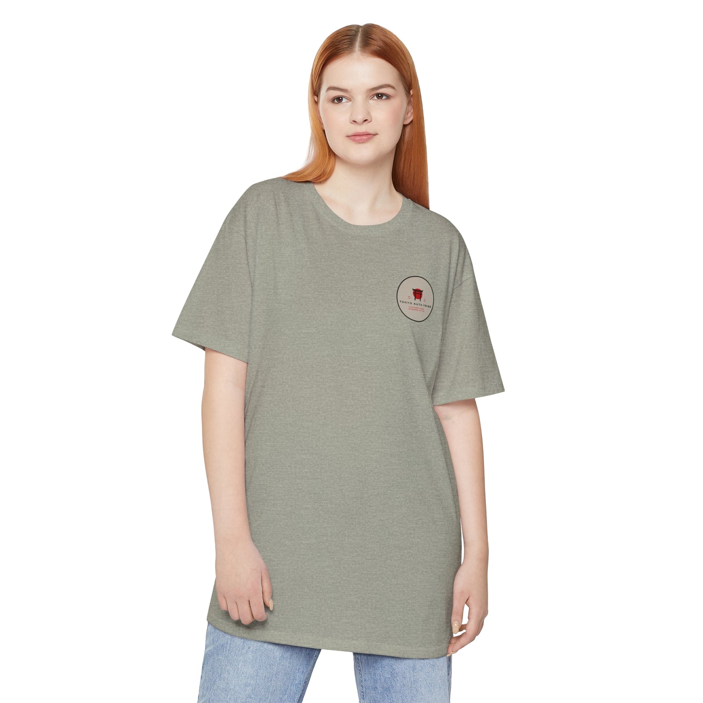 Model wearing a muted green Unbreakable Spirit oversized T-Shirt with a small graphic on the chest, styled casually with light blue jeans, reflecting JDM streetwear inspired by Japanese car culture.
