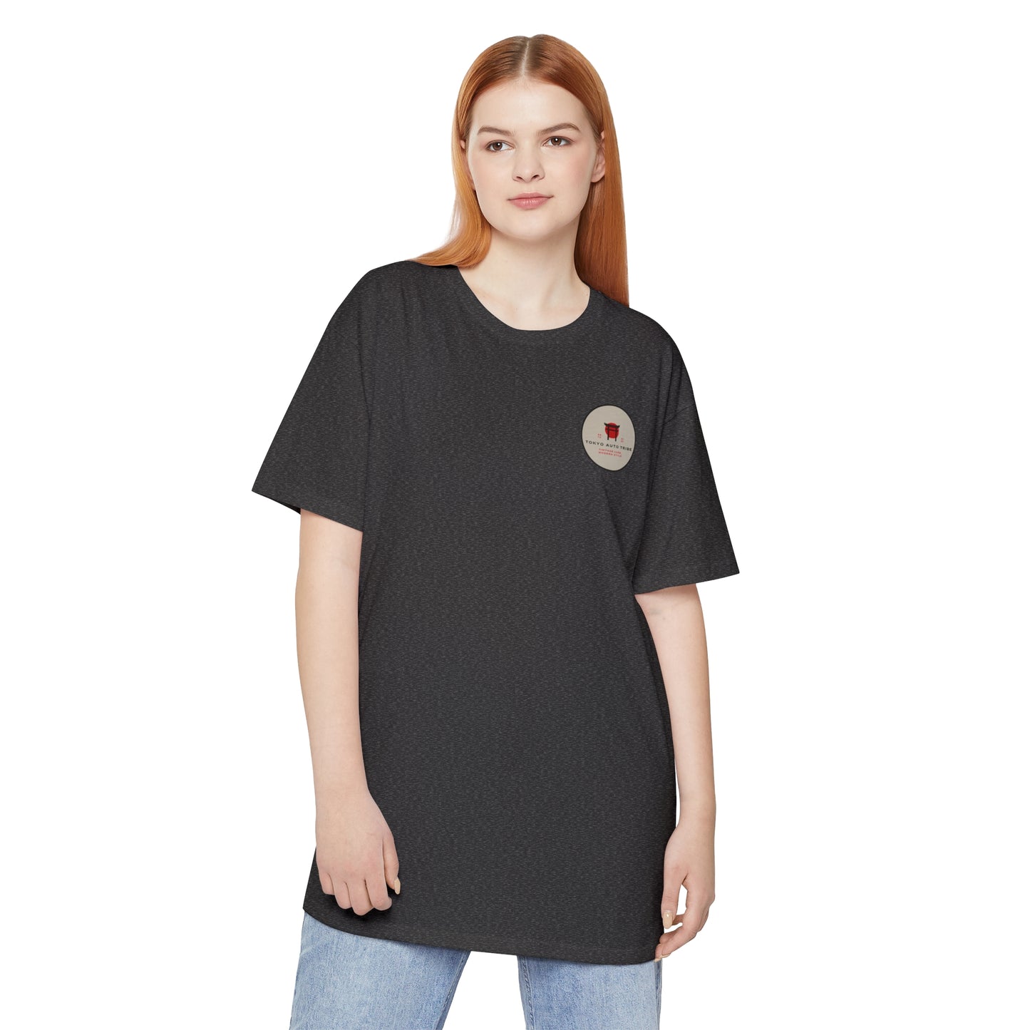 Young woman wearing a black Unbreakable Spirit oversized T-Shirt with a small circular logo on the chest, styled with casual light blue jeans, embodying automotive streetwear inspired by Japanese car culture.