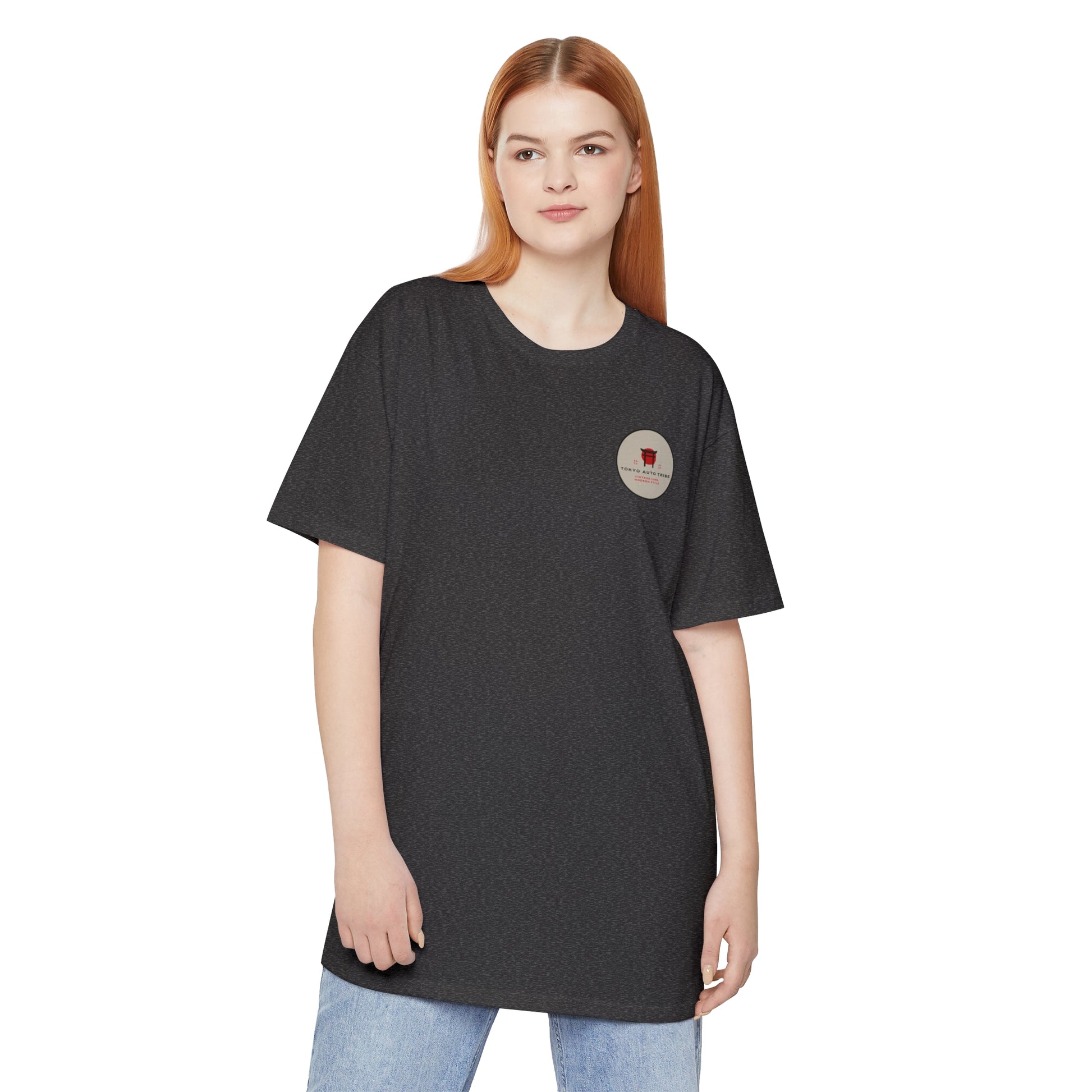 Young woman wearing a black Unbreakable Spirit oversized T-Shirt with a small circular logo on the chest, styled with casual light blue jeans, embodying automotive streetwear inspired by Japanese car culture.