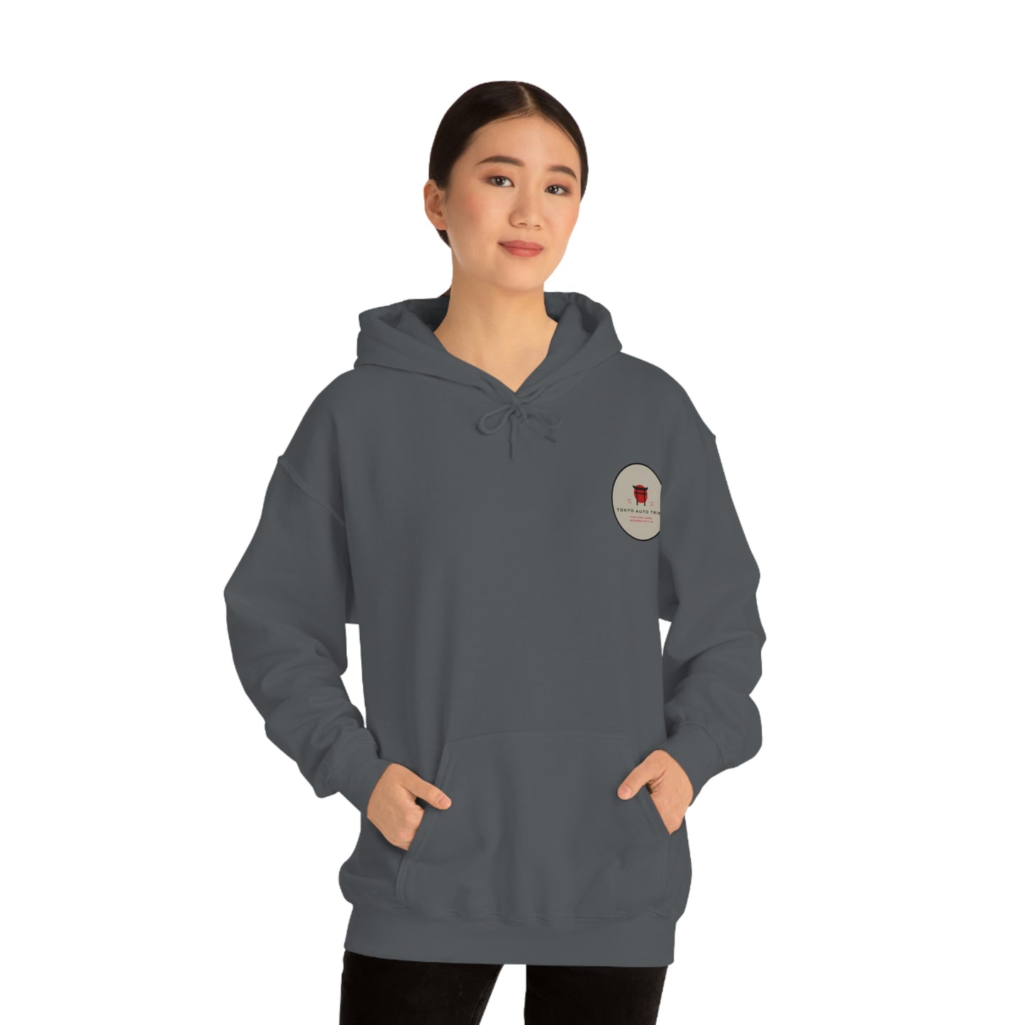 Woman wearing a dark hoodie with a small logo on the chest, standing with hands in pockets and modeling the Groovy Grocery Runner Hoodie, capturing a relaxed automotive-inspired streetwear style.