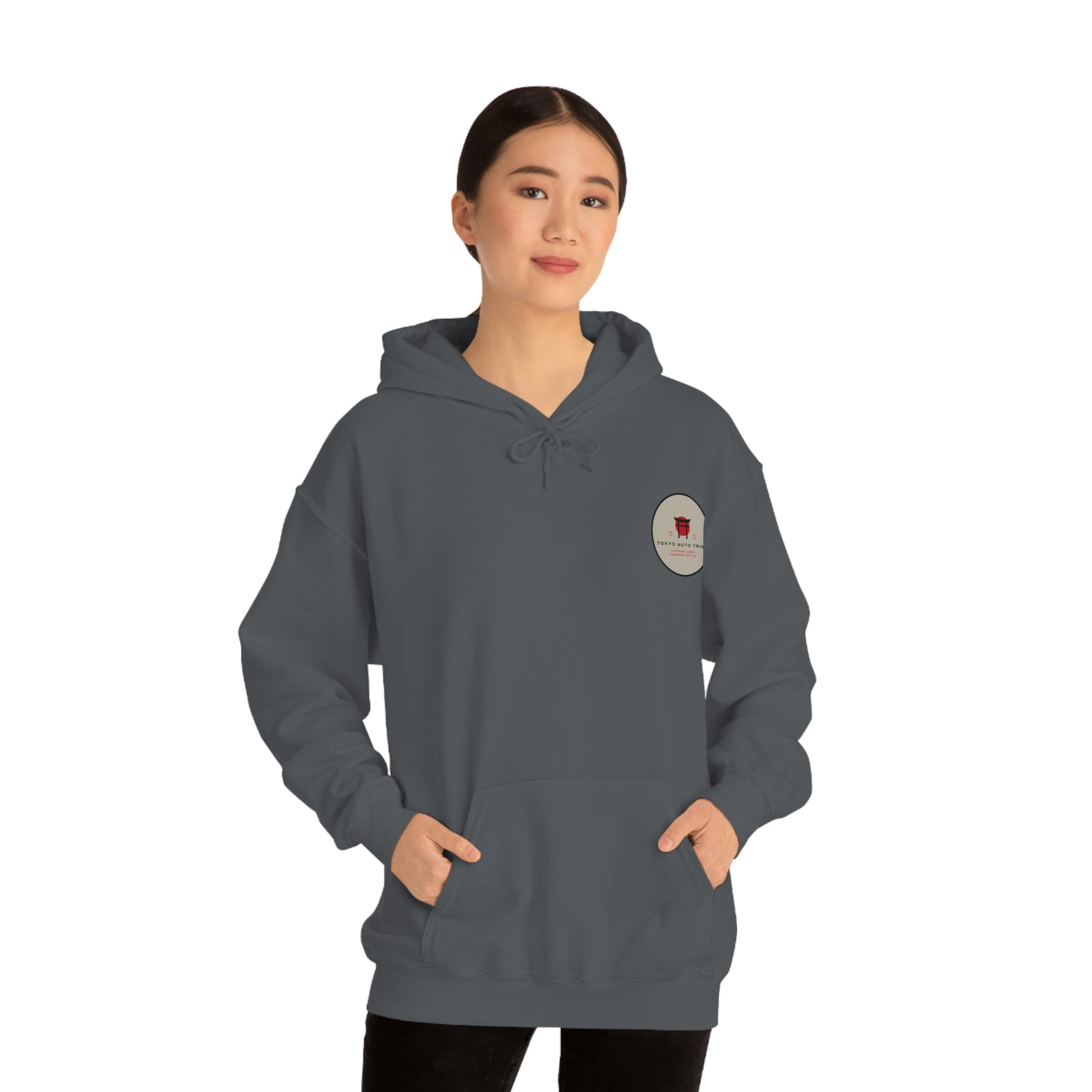 Woman wearing a dark hoodie with a small logo on the chest, standing with hands in pockets and modeling the Groovy Grocery Runner Hoodie, capturing a relaxed automotive-inspired streetwear style.