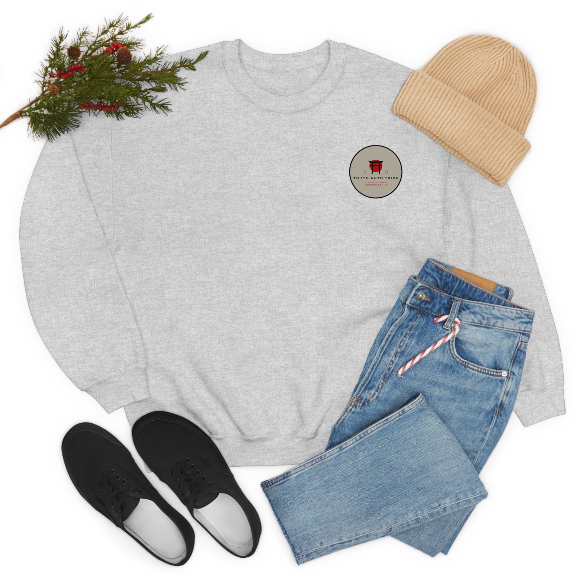 Light gray Wagon Chibi Sweater featuring a small red graphic on the chest, styled with blue jeans, black shoes, a beige beanie, and festive greenery nearby.