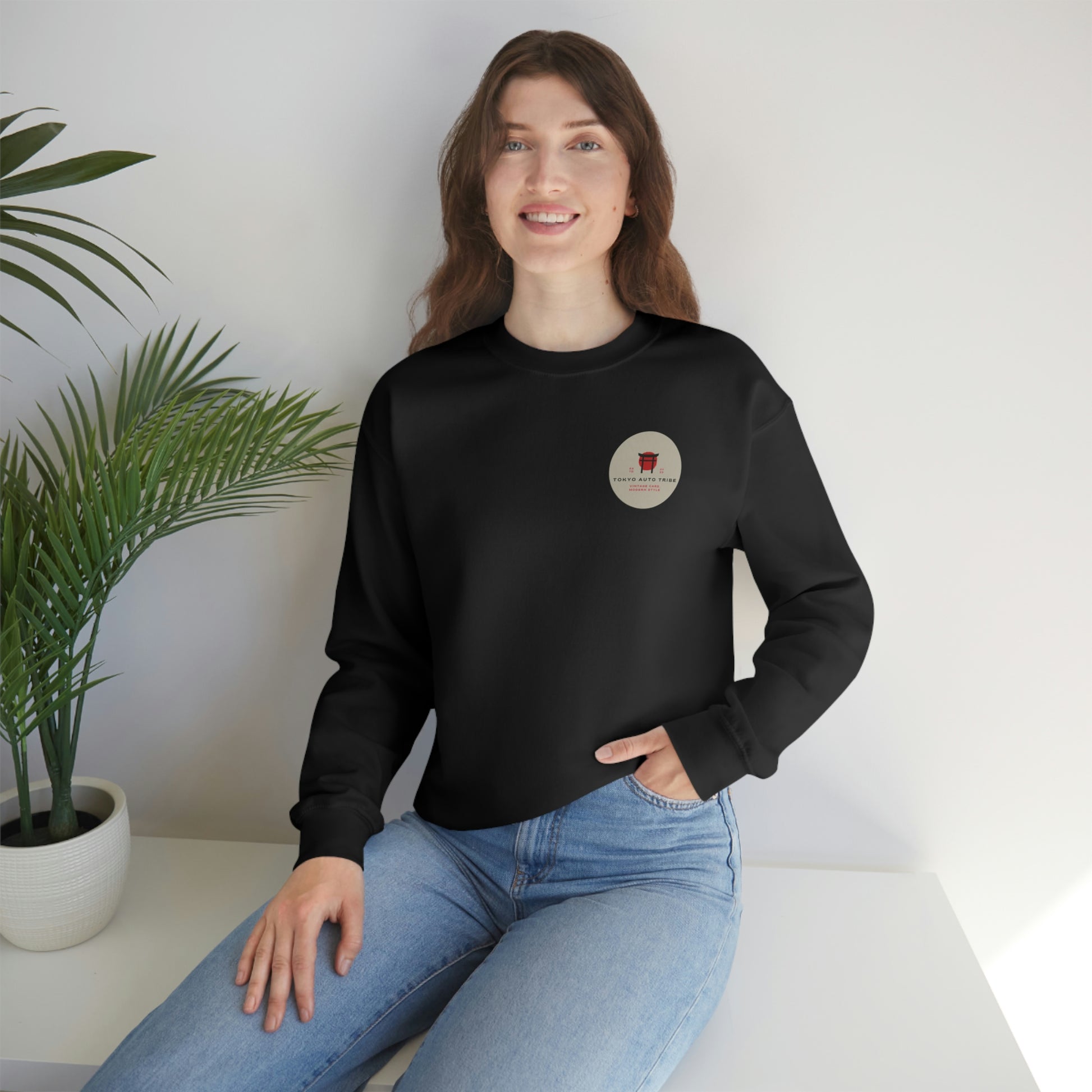Woman wearing The Family Wagon Sweater in black with a small vintage Japanese car culture graphic on the chest, styled casually with light blue jeans in a bright, minimal setting.