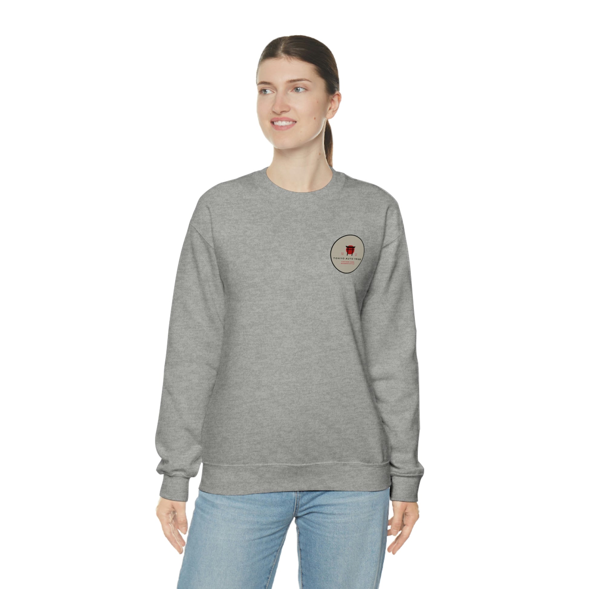 Woman wearing a gray crewneck sweatshirt featuring a small graphic on the chest, styled casually with blue jeans, showcasing The Family Wagon Sweater designed for fans of Japanese car culture and late-night drives.