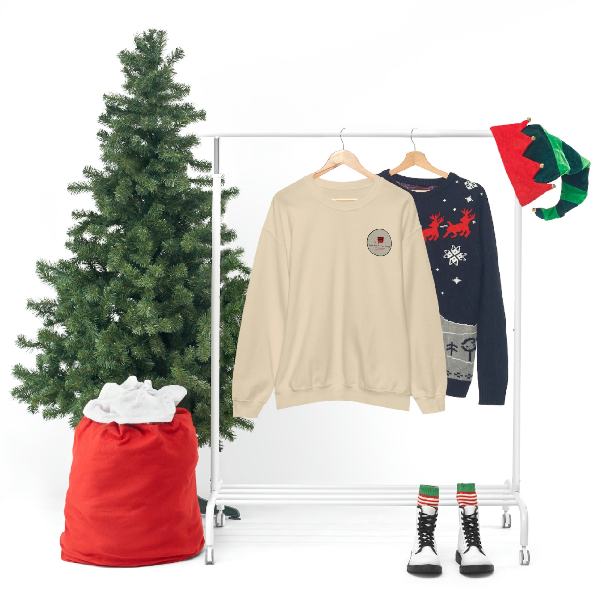 The Family Wagon Sweater in beige hangs next to a navy blue holiday sweater with red reindeer, surrounded by festive Christmas tree, red sack, elf hats, and striped socks with boots.