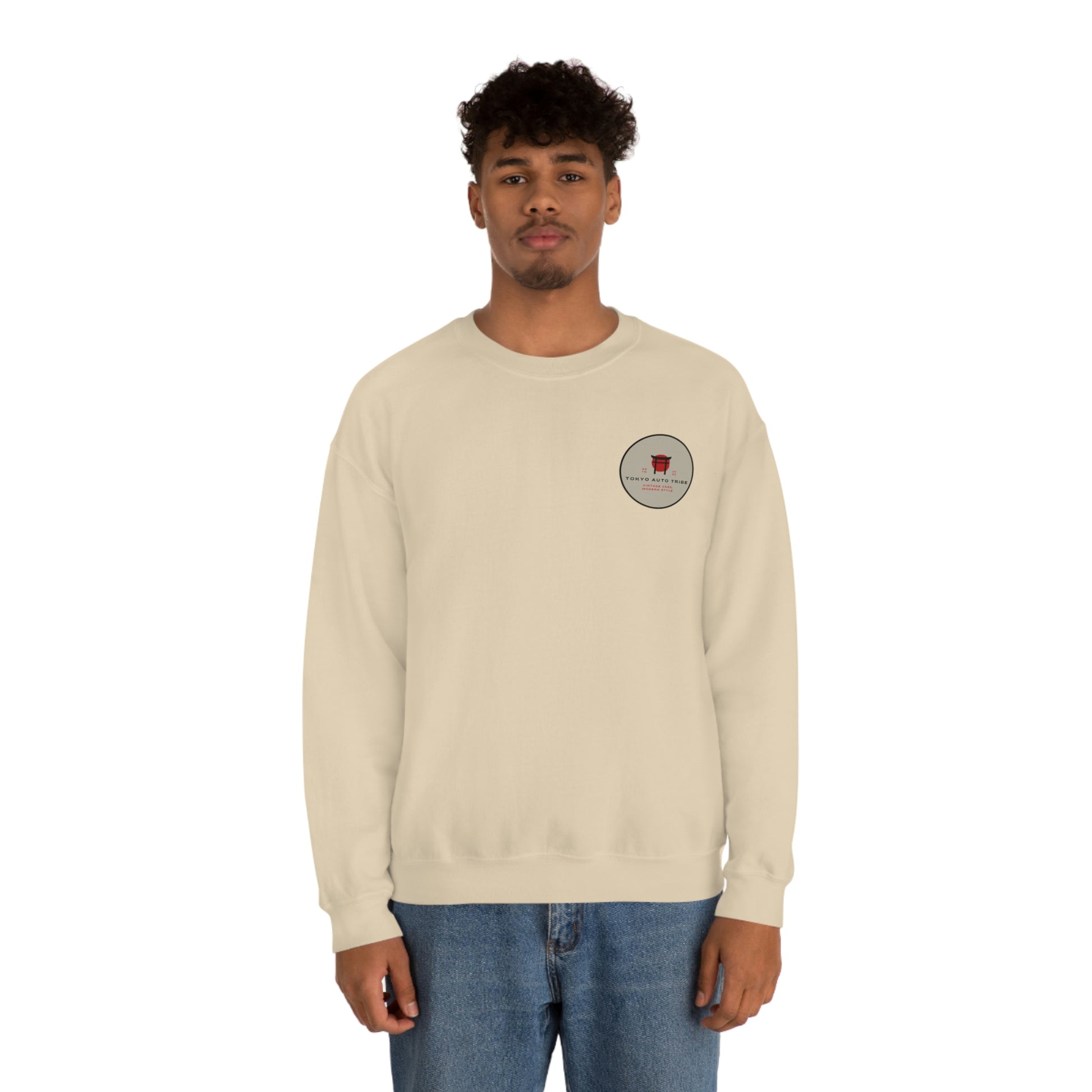 A man wearing The Family Wagon Sweater in a light beige color featuring subtle Tokyo Auto Tribe branding, styled casually with blue jeans against a plain background.
