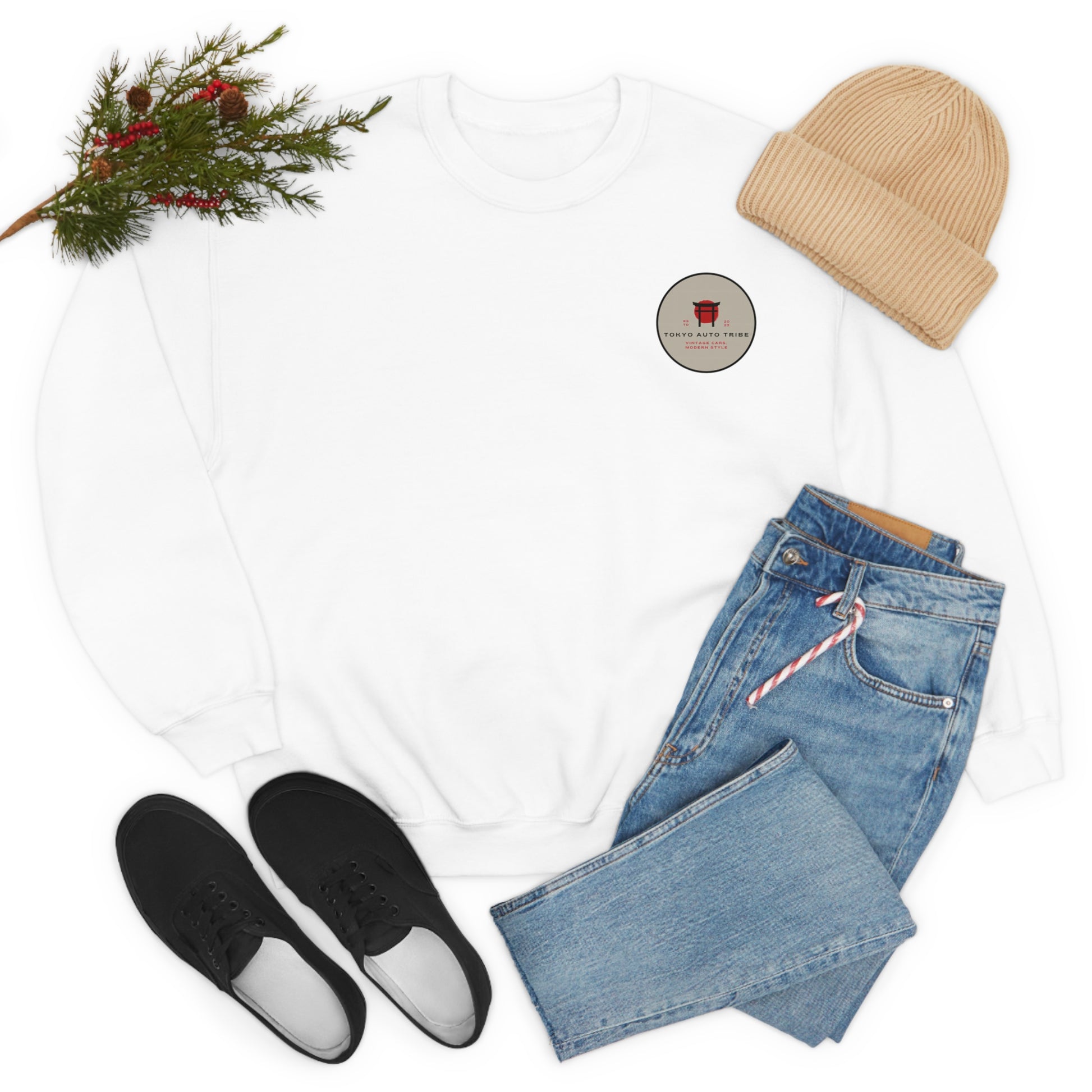 White Wagon Chibi Sweater laid flat with small round car culture graphic on chest paired with light blue jeans, black sneakers, beige knit beanie, and sprig of greenery for a casual JDM streetwear look.