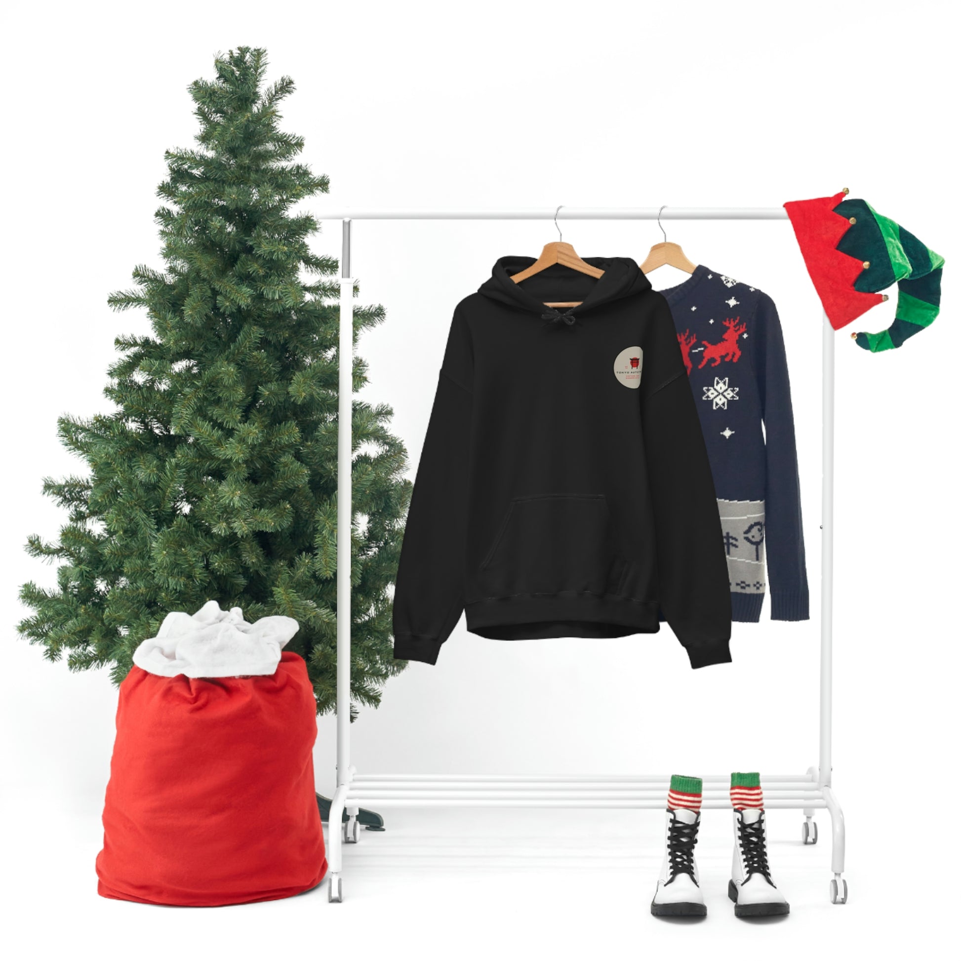 Black hoodie with a small graphic on the chest hanging next to a festive holiday sweater on a white clothing rack, accompanied by Christmas decorations including a green tree, red sack, and elf hat, featuring Godzilla's Fury Hoodie.