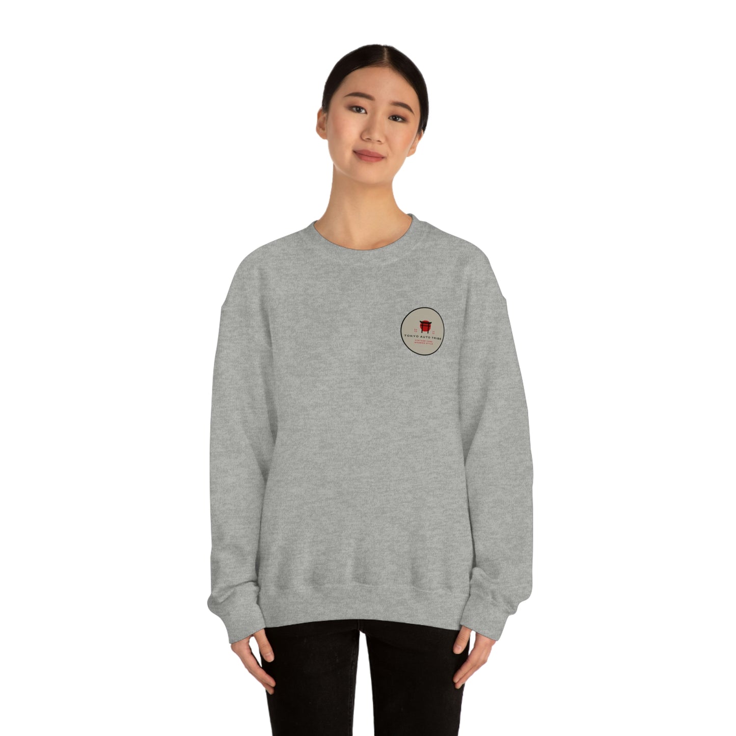 Young woman wearing a grey crewneck sweatshirt with a small circular logo on the chest, showcasing The Family Wagon Sweater designed for fans of Japanese car culture and late-night drives.