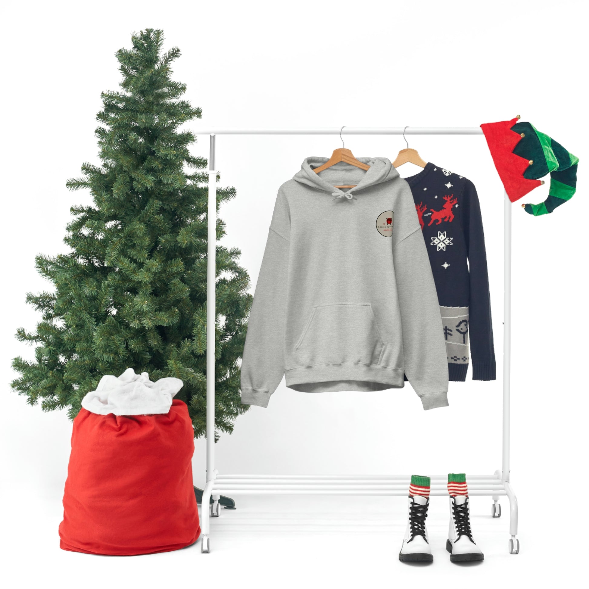 Groovy Grocery Runner Hoodie in gray hanging on a rack alongside a festive navy sweater, holiday boots, elf hats, and a small Christmas tree with a red sack, capturing a cozy winter vibe.