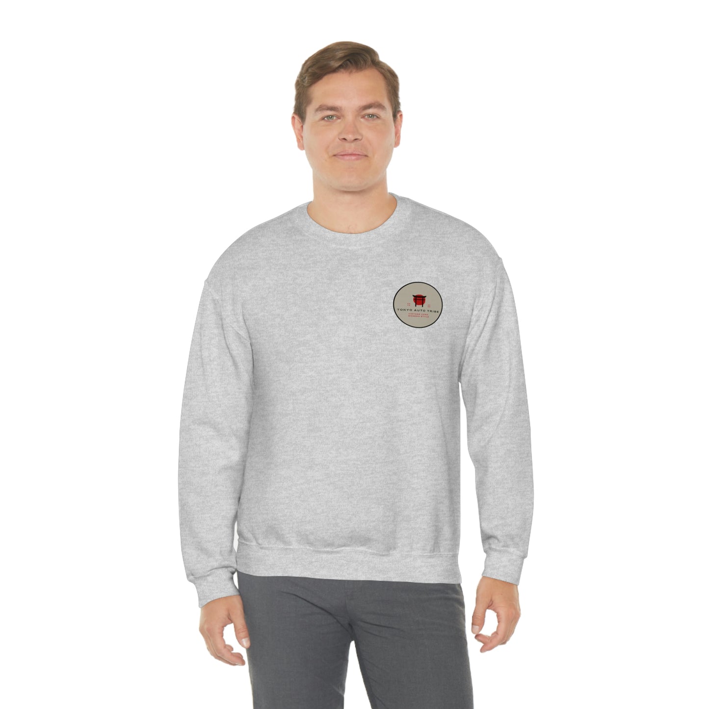 Man wearing a light gray crewneck sweatshirt featuring a small circular graphic on the chest, showcasing The Family Wagon Sweater with a clean and casual style inspired by Japanese car culture.