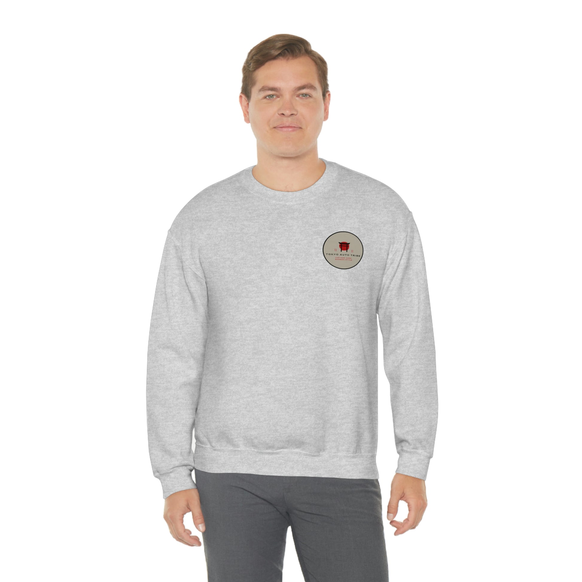 Man wearing a light gray crewneck sweatshirt featuring a small circular graphic on the chest, showcasing The Family Wagon Sweater with a clean and casual style inspired by Japanese car culture.