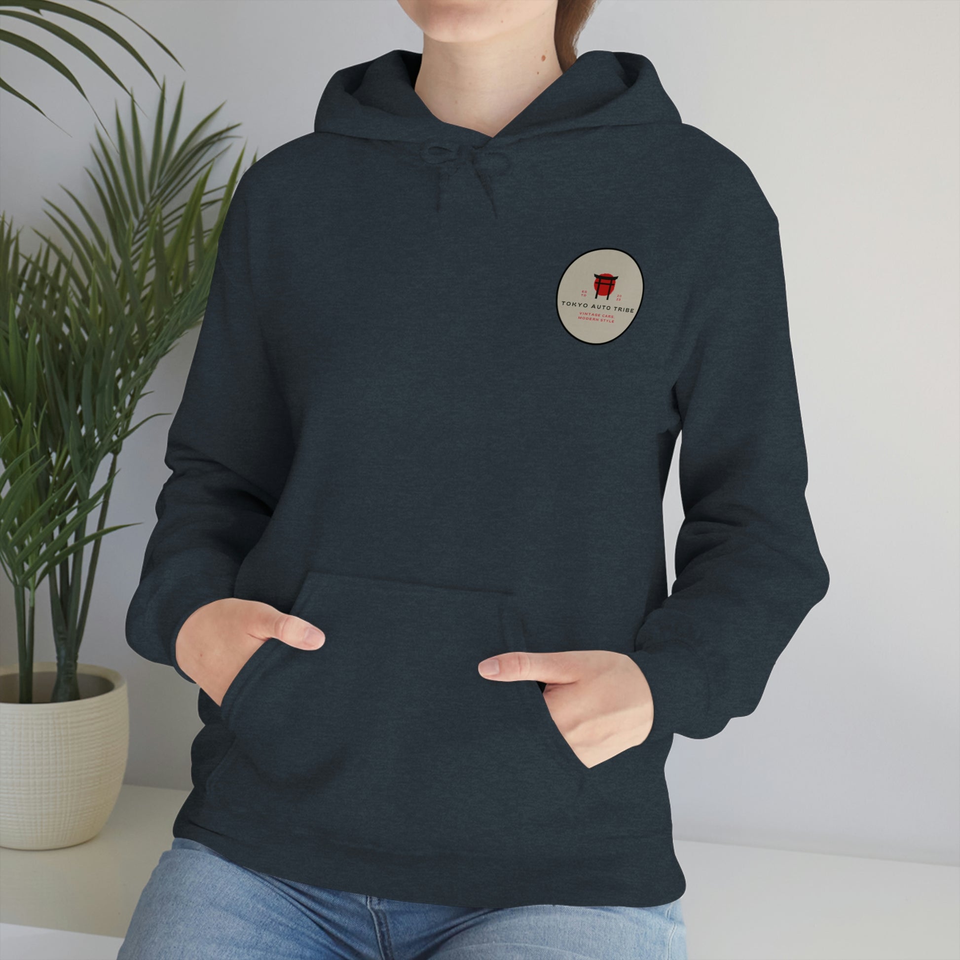 Person wearing a dark hoodie with a small red grocery cart graphic and text badge on the chest, styled as the Groovy Grocery Runner Hoodie, blending casual comfort with a nod to Japanese car culture.
