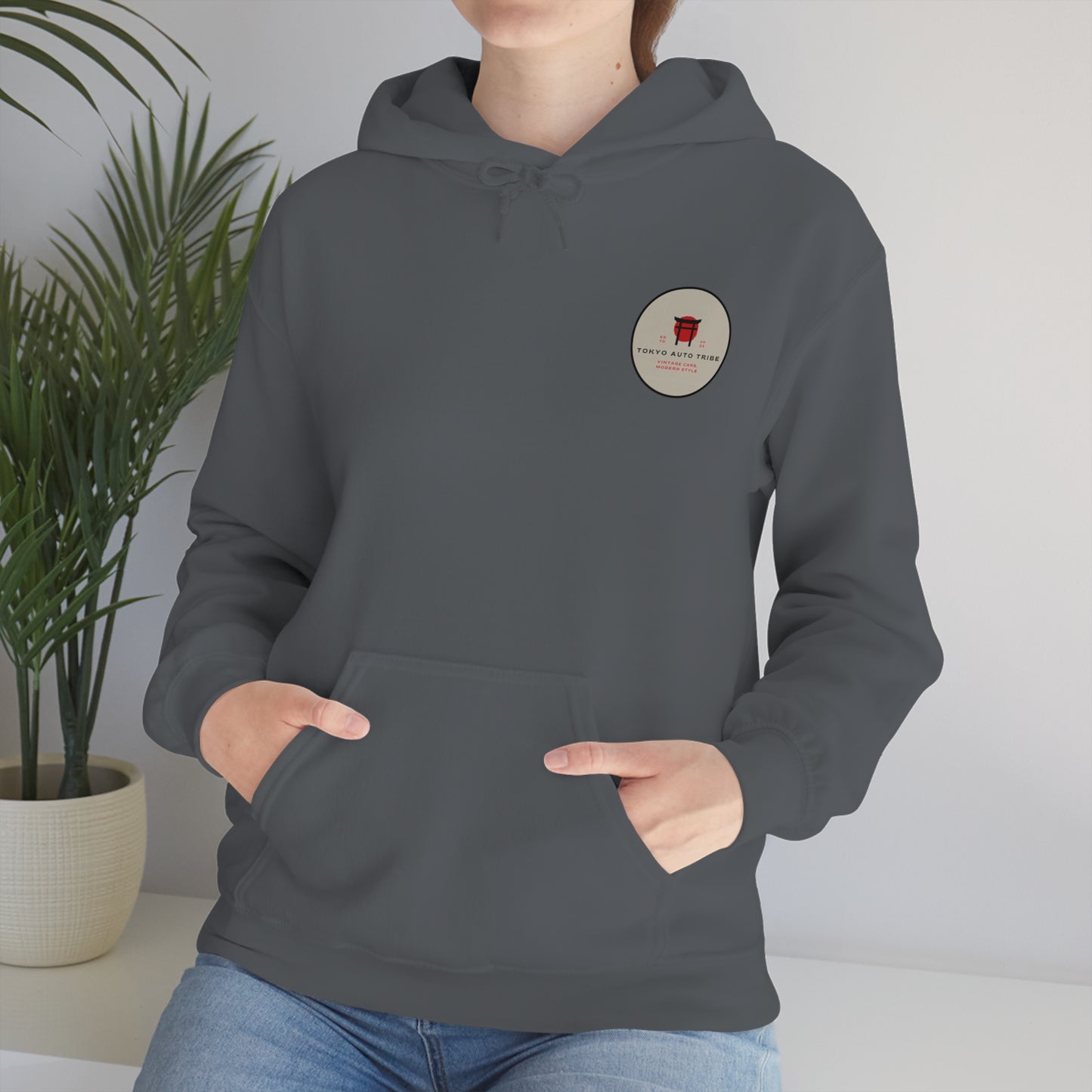 Person wearing a dark gray Wagon Chibi Hoodie featuring a small circular Japanese car culture graphic on the chest, styled for fans of late-night drives and tuner streetwear.