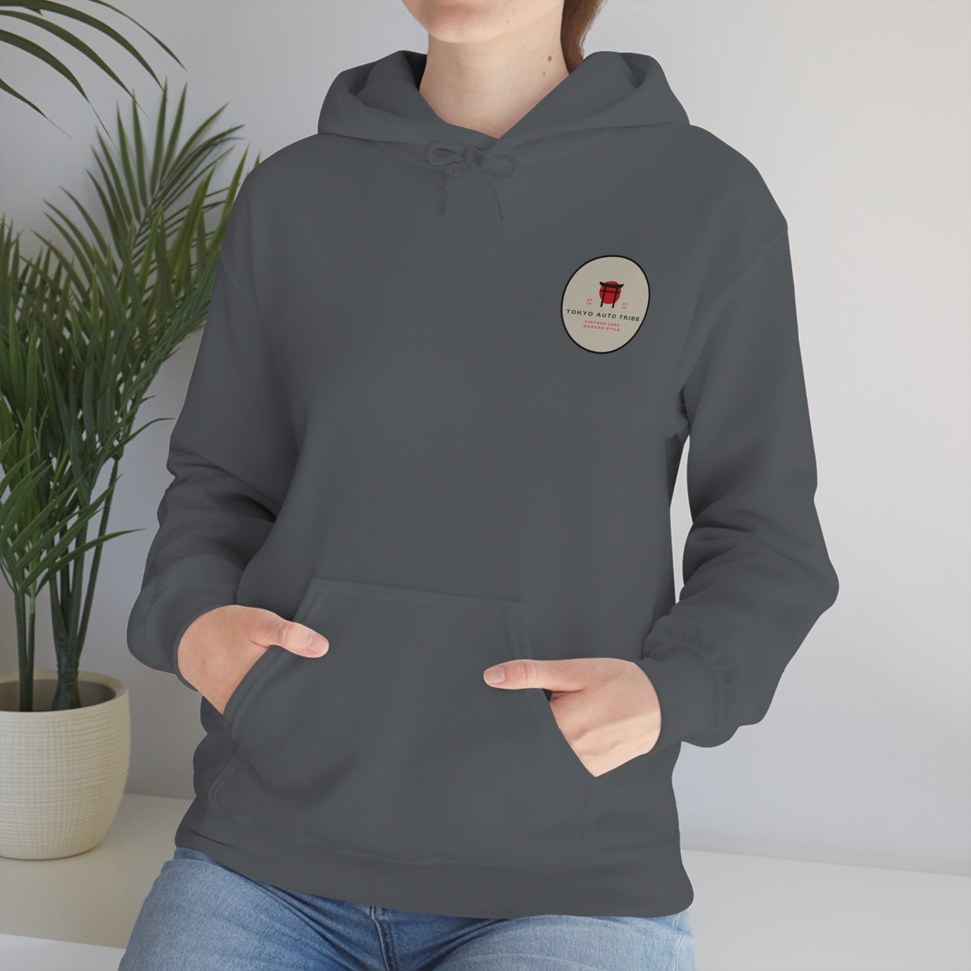 Person wearing a dark gray Wagon Chibi Hoodie featuring a small circular Japanese car culture graphic on the chest, styled for fans of late-night drives and tuner streetwear.