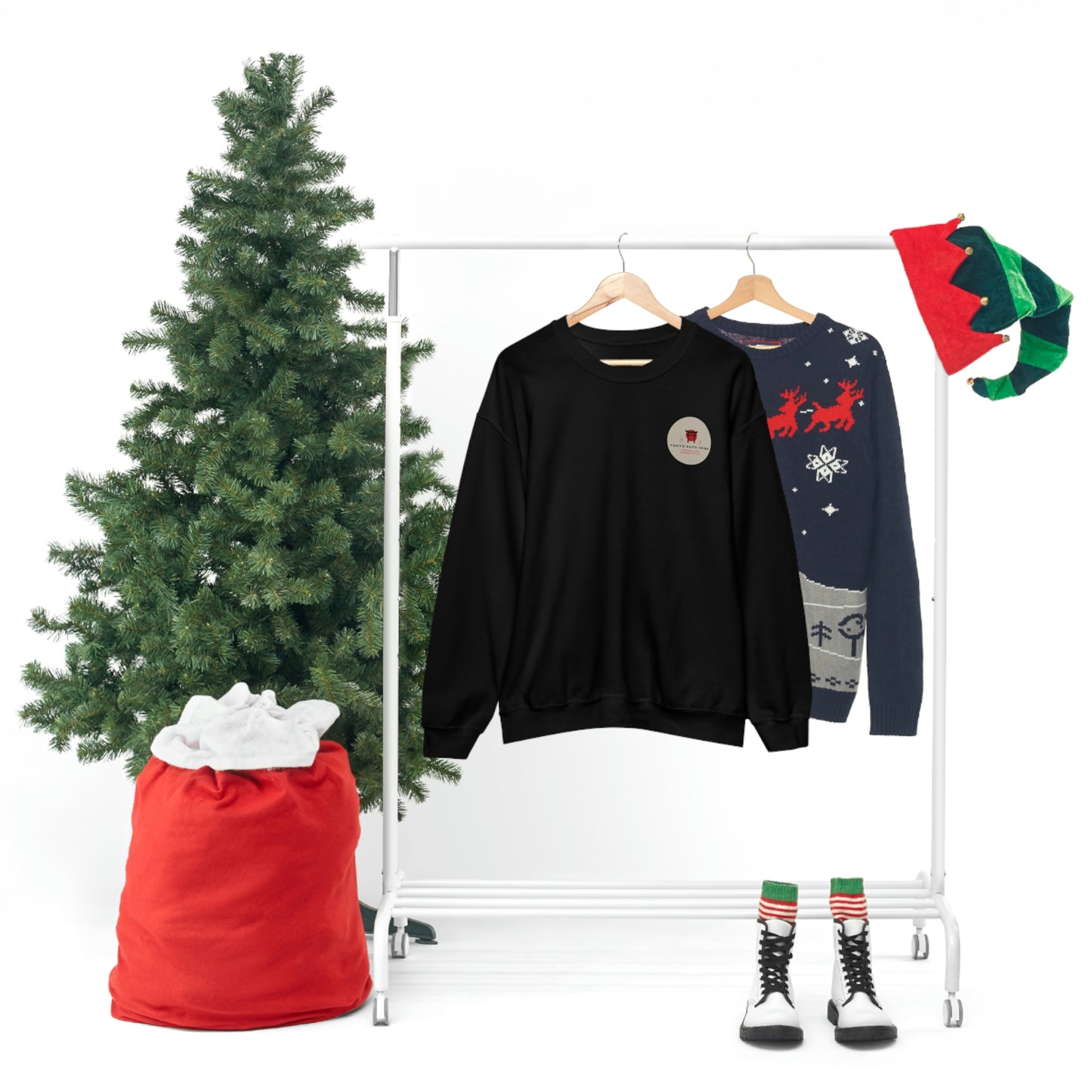 The Family Wagon Sweater black crewneck with subtle logo next to holiday-themed navy sweater, surrounded by festive Christmas tree, stocking, elf hat, and winter boots.