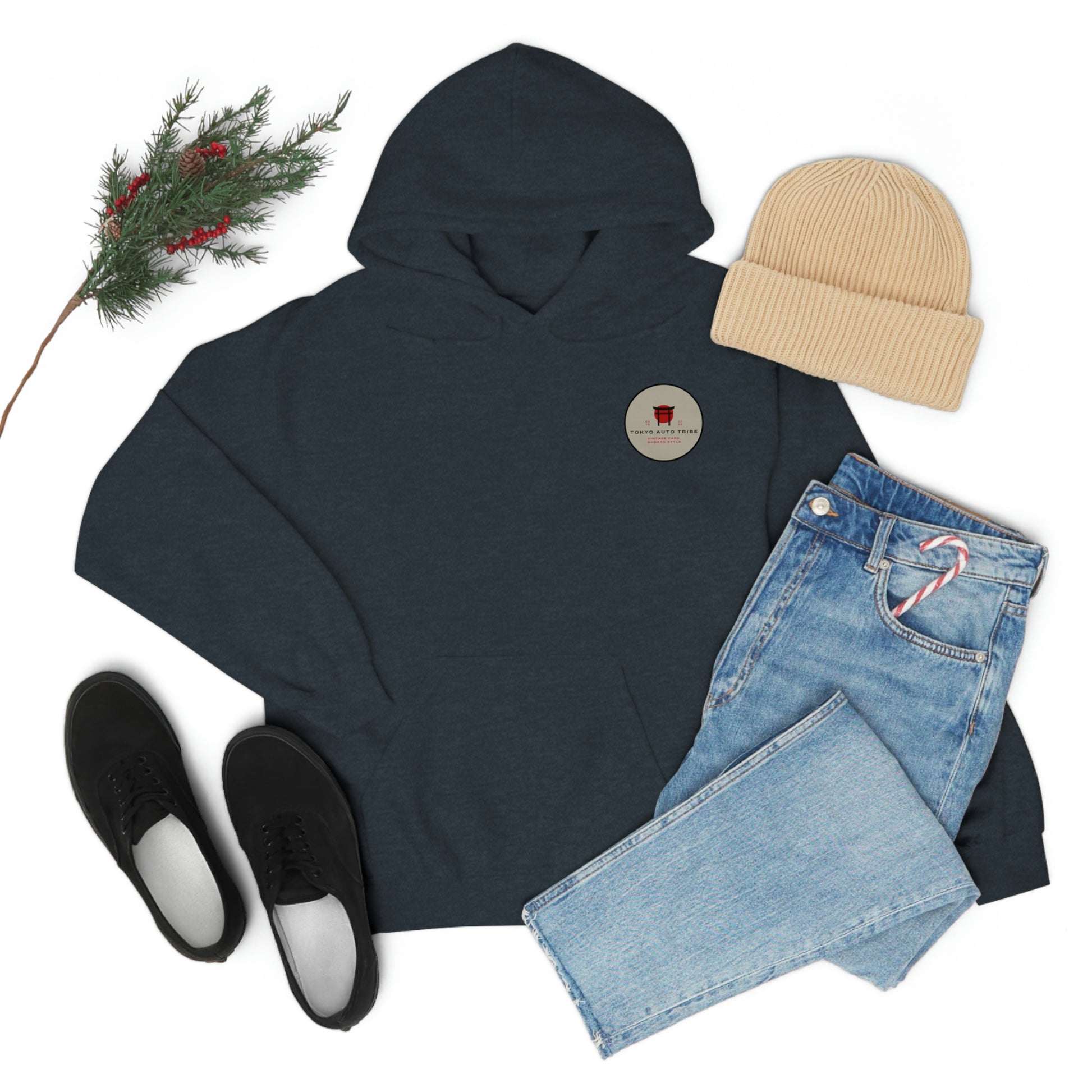 Dark hoodie with a small round patch paired with light blue jeans holding a candy cane, black slip-on shoes, and a beige knit beanie, styled with festive greenery, showcasing Godzilla's Fury Hoodie built for Japanese car culture enthusiasts.