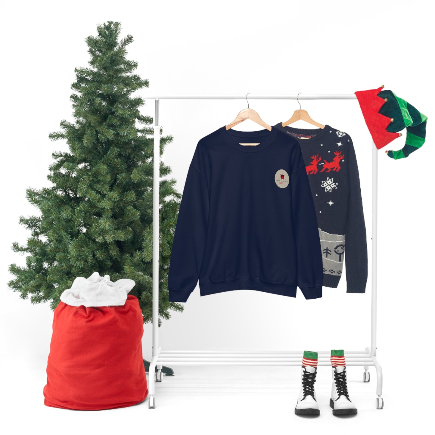 Two Wagon Chibi Sweaters hanging on wooden hangers on a white clothing rack next to a decorated Christmas tree, a large red sack, and elf-themed boots and hats arranged for a festive display.