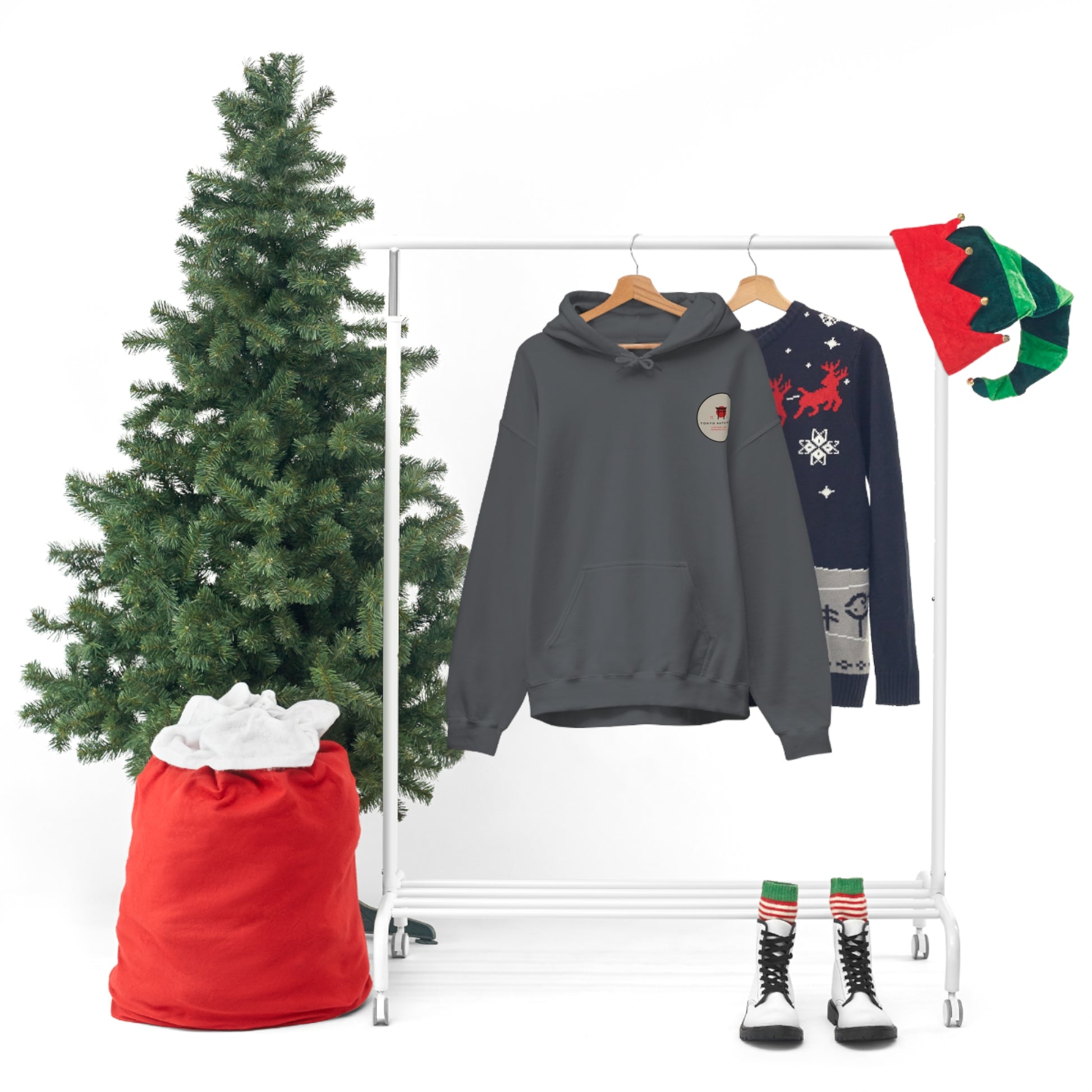 Wagon Chibi Hoodie in dark gray hanging on a rack next to a festive sweater, surrounded by holiday decorations including a Christmas tree, red sack, elf hats, and striped socks with boots, embodying Japanese car culture vibes.
