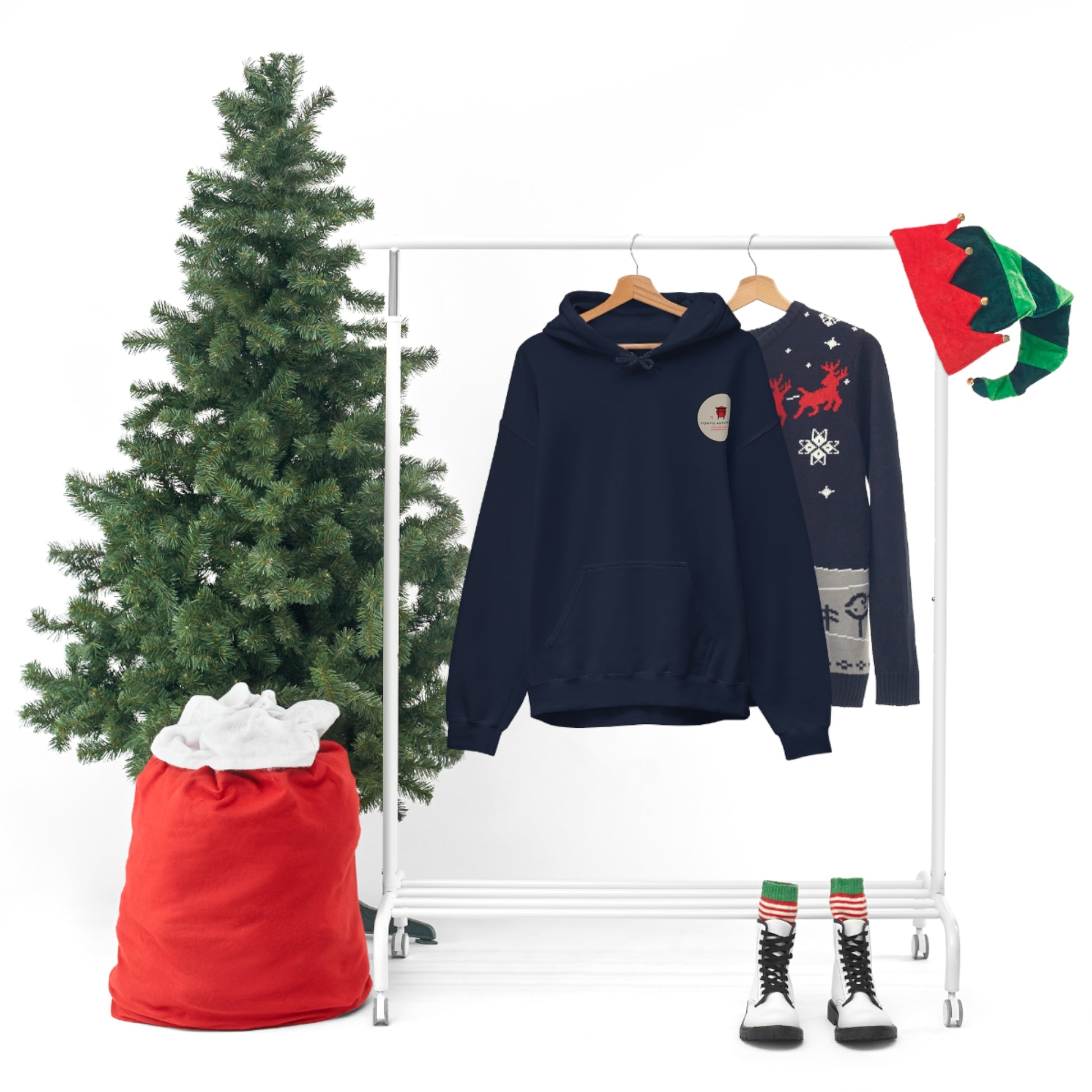 Wagon Chibi Hoodie displayed on a hanger beside a festive Christmas sweater, a small artificial tree, a large red sack, and holiday elf hats, capturing a cozy holiday vibe.