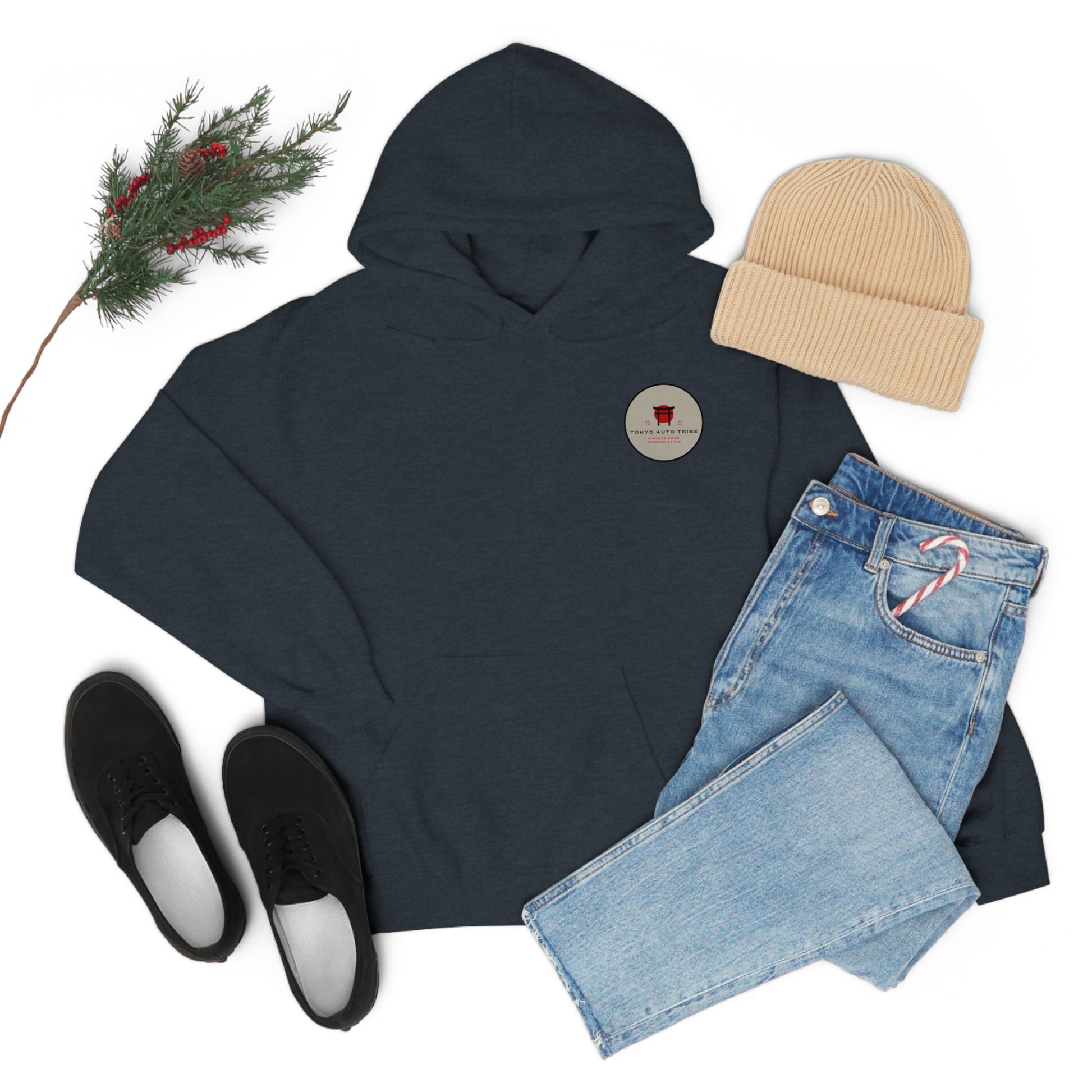 Dark navy Wagon Chibi Hoodie styled with folded light blue jeans holding a candy cane, beige ribbed knit beanie, black slip-on shoes, and a sprig of pine and red berries, representing Japanese car culture and late-night drives.