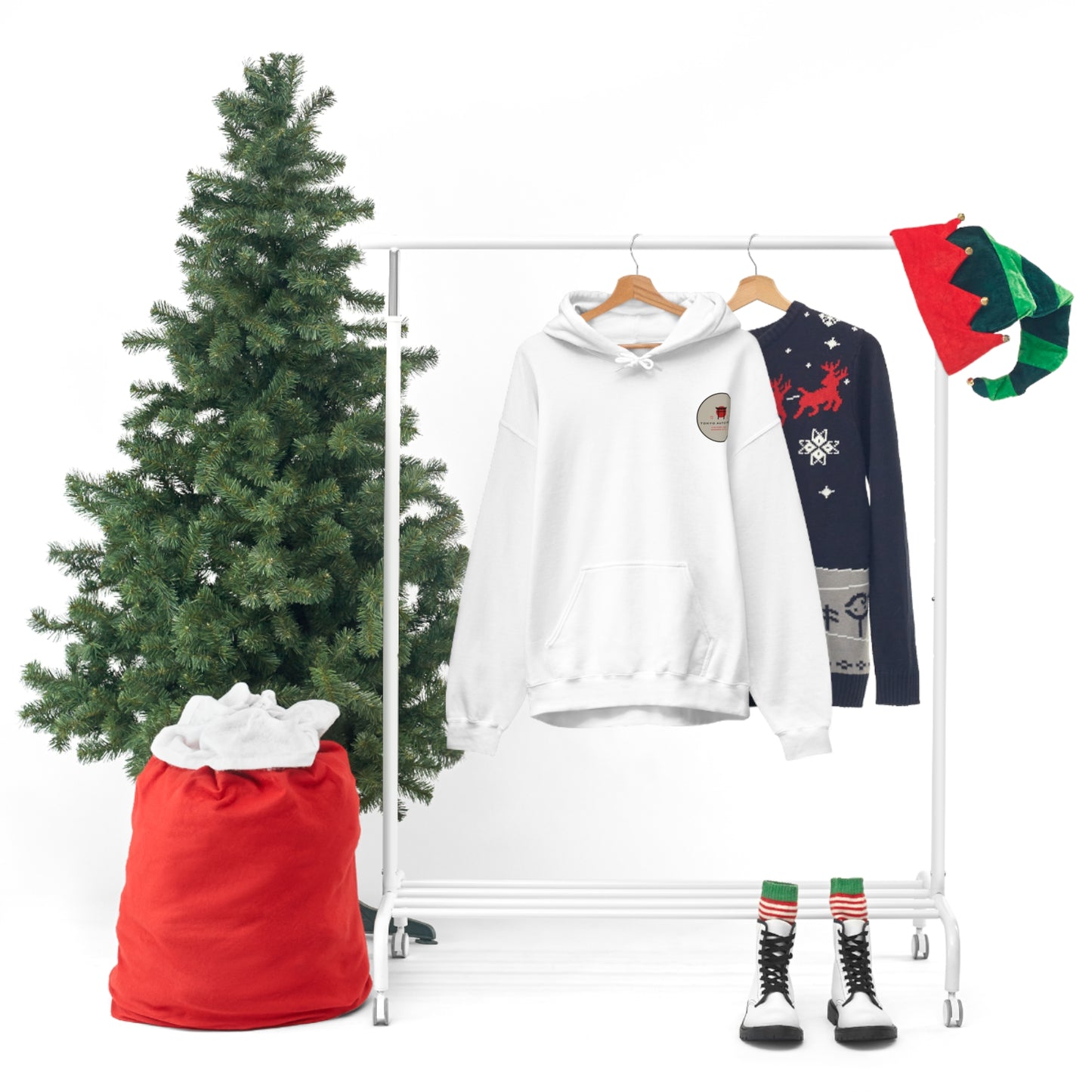 Wagon Chibi Hoodie in white hanging on a rack next to a festive holiday sweater, Christmas tree, red sack, elf hats, and striped winter boots, capturing winter and tuner culture vibes.
