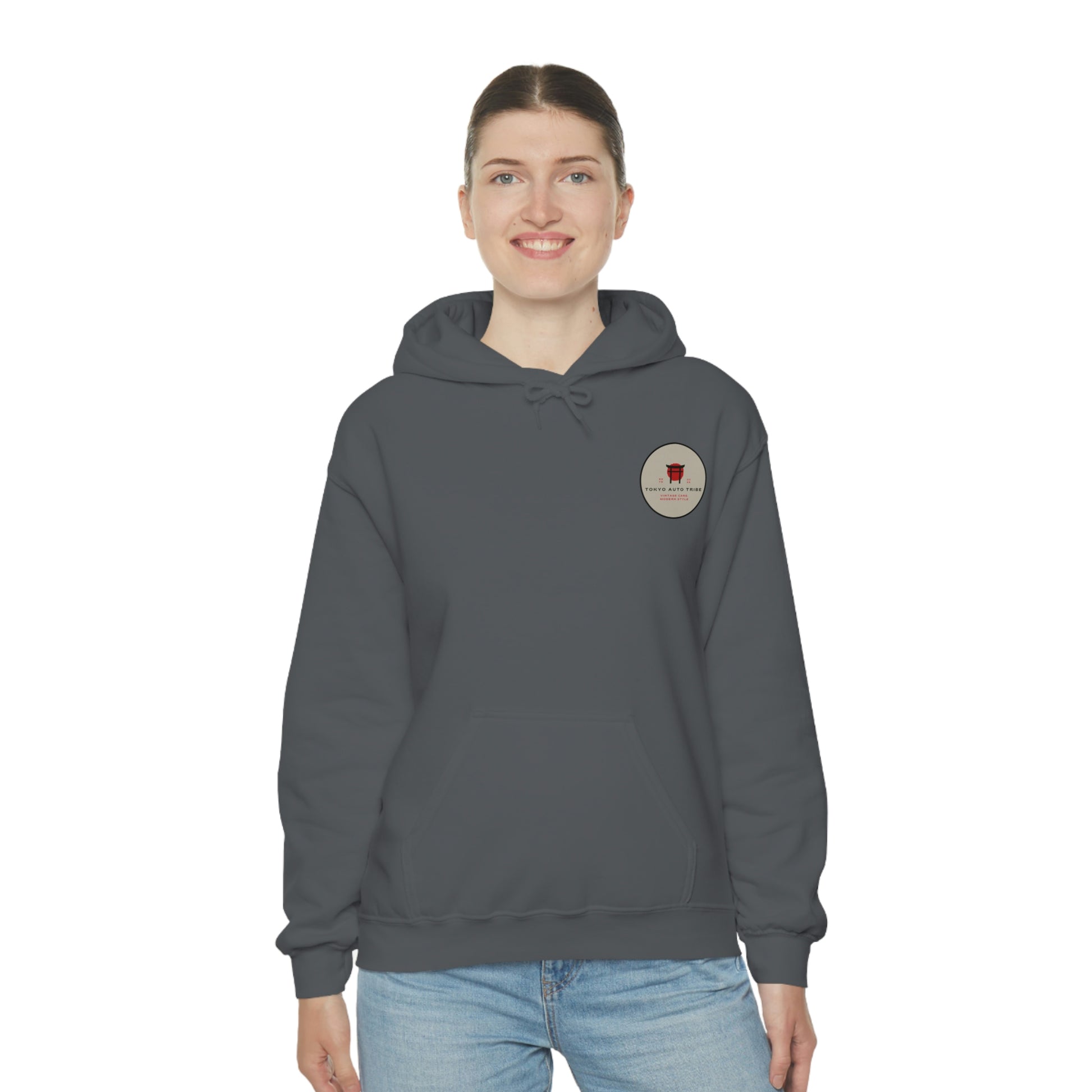 Smiling woman wearing a dark gray Groovy Grocery Runner Hoodie featuring a small round automotive graphic on the chest, embodying Tokyo Auto Tribe’s streetwear inspired by Japanese car culture and late-night drives.