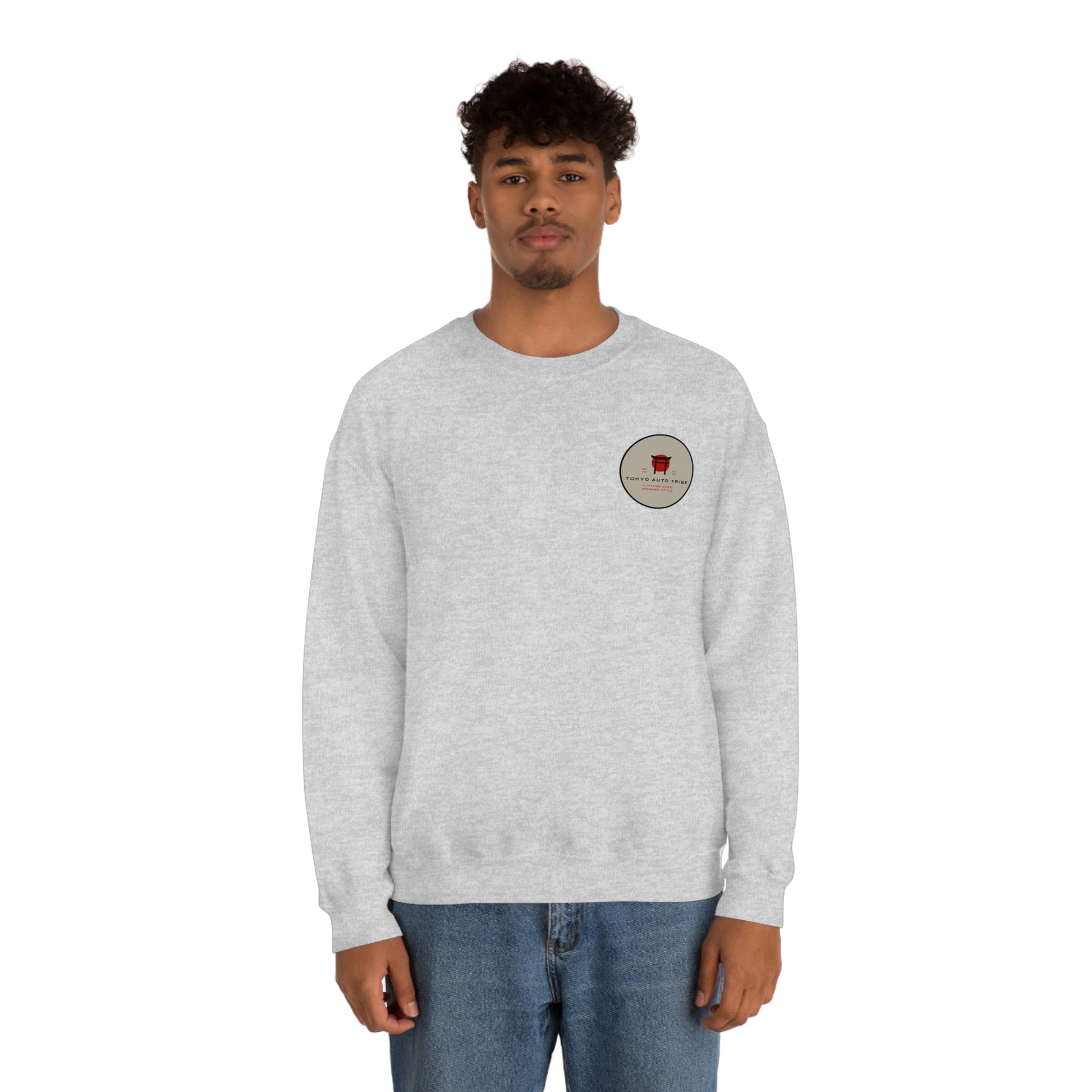 Man wearing a light gray crewneck sweatshirt with a small vintage-style graphic on the chest, showcasing The Family Wagon Sweater designed for fans of Japanese car culture and late-night drives.